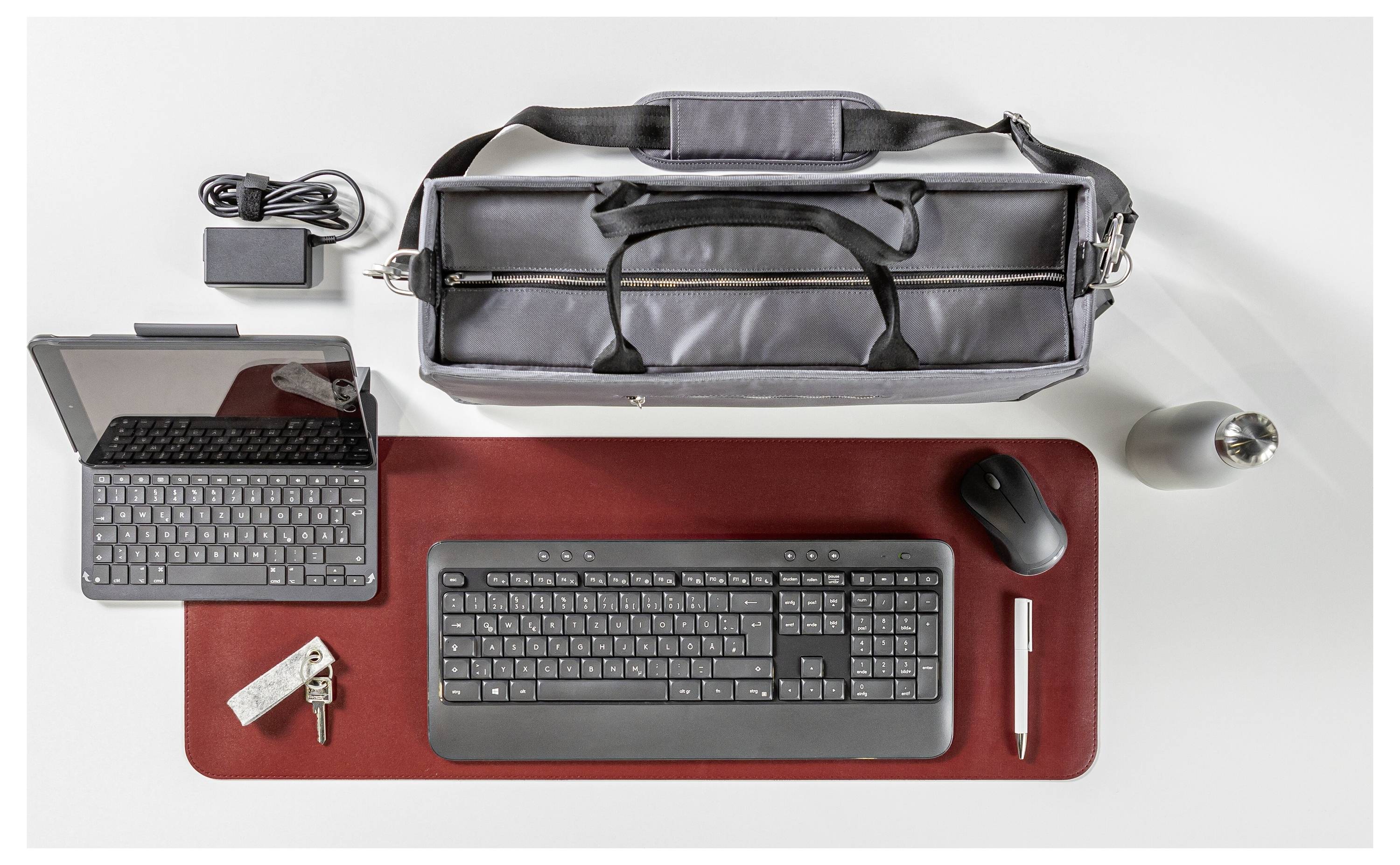 Laptoptasche, Laptop, Tastatur, Maus, Ladegerät, Stift, Flasche und Schlüssel ordentlich auf einem Tisch angeordnet.