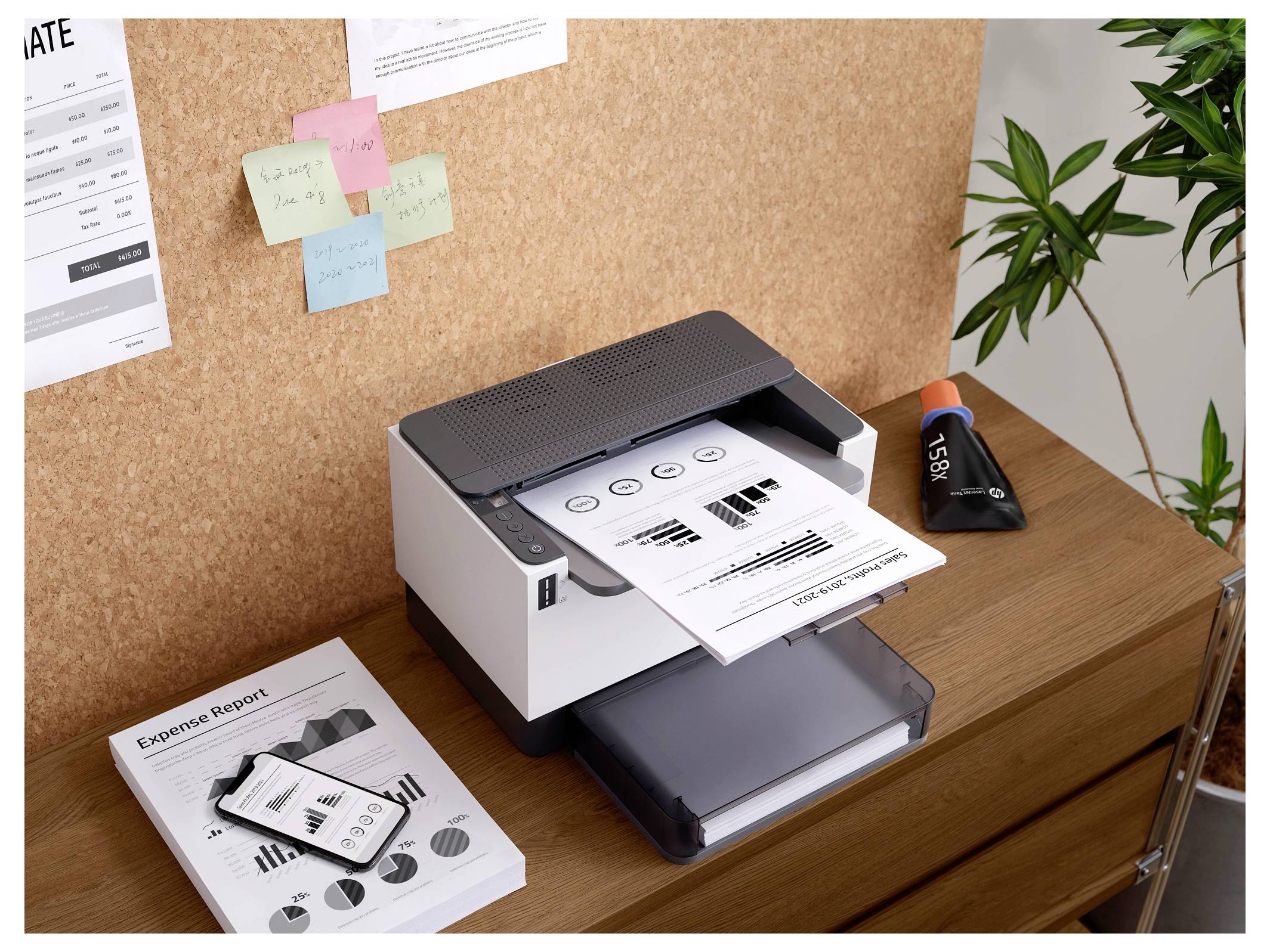 Ein Desktop-Drucker druckt einen Geschäftsbericht in Graustufen mit Balken- und Kreisdiagrammen. In der Nähe befinden sich gedruckte und digitale Berichte sowie Haftnotizen an einer Pinnwand.