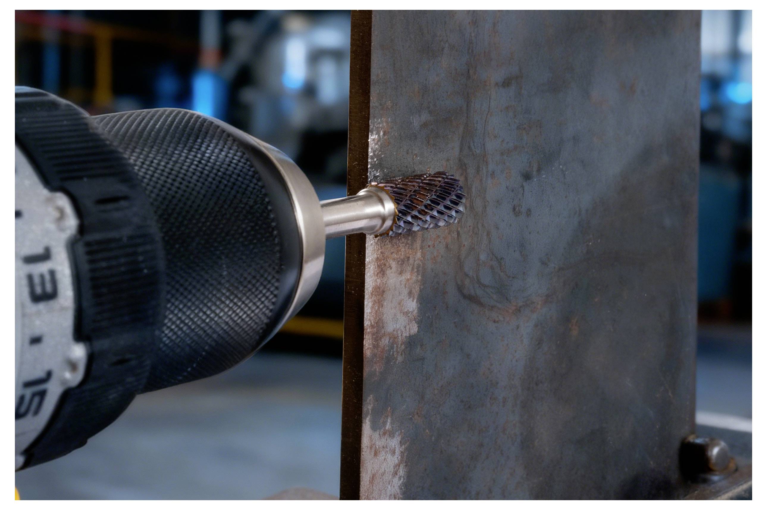 Eine Bohrmaschine mit einem Bürstenaufsatz glättet die Kante eines Metallblechs in einer industriellen Umgebung.