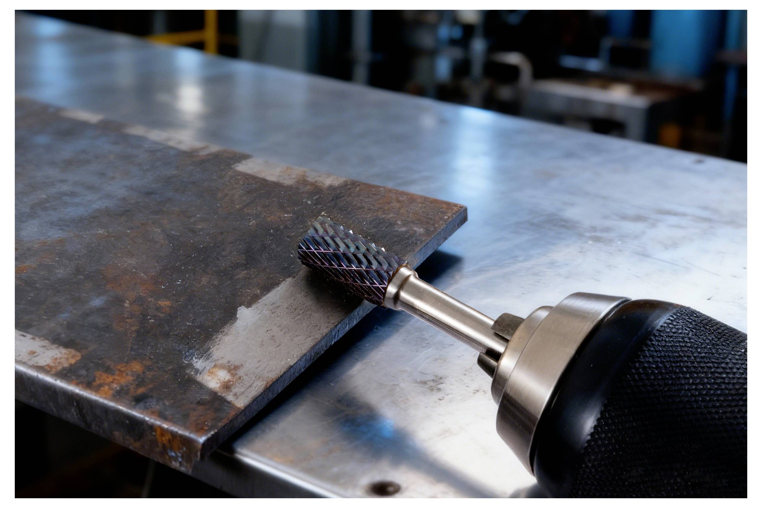 Ein handgehaltenes Rotationswerkzeug poliert die Kante eines Metallblechs auf einer Werkbank, was auf industrielle Metallbearbeitung oder Fertigung hinweist.