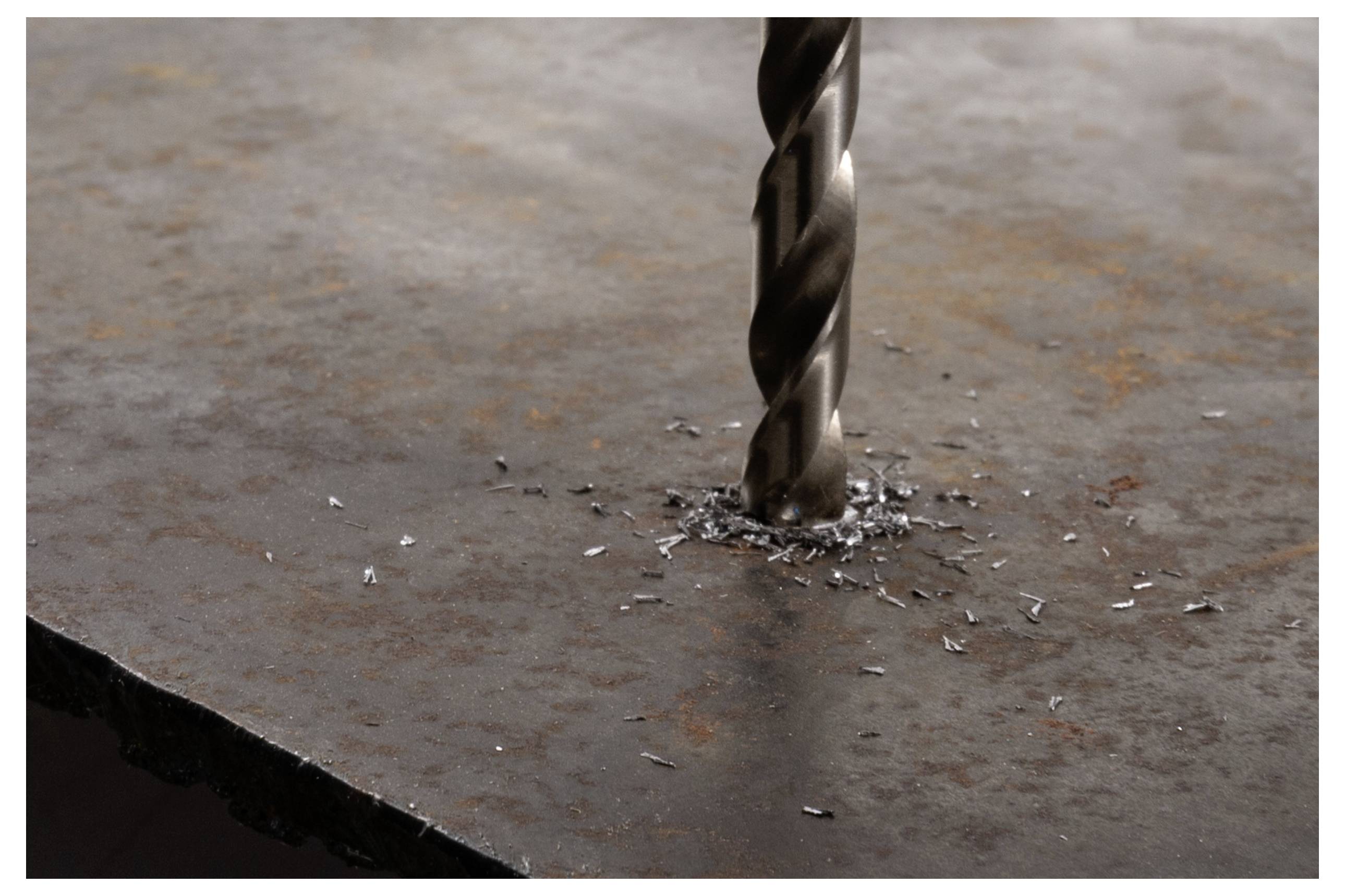 Ein Metallbohrer bohrt in eine rostige Metalloberfläche und erzeugt kleine Späne um das Loch herum.