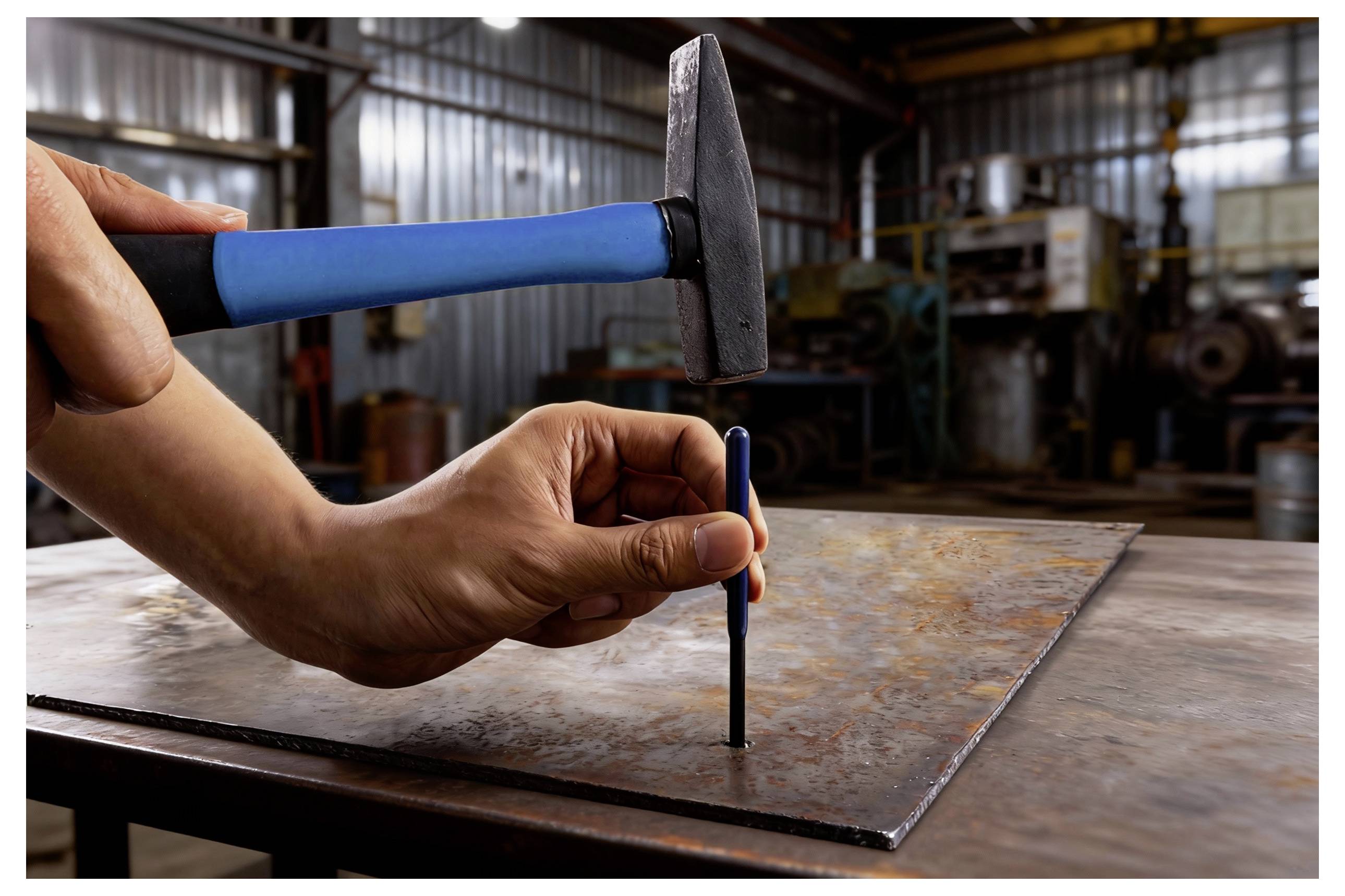 Eine Person benutzt einen blauen und schwarzen Hammer, um einen Metallstempel auf ein rostiges Metallblech in einer Werkstatt zu schlagen, was Handwerkskunst oder Metallbearbeitung andeutet.