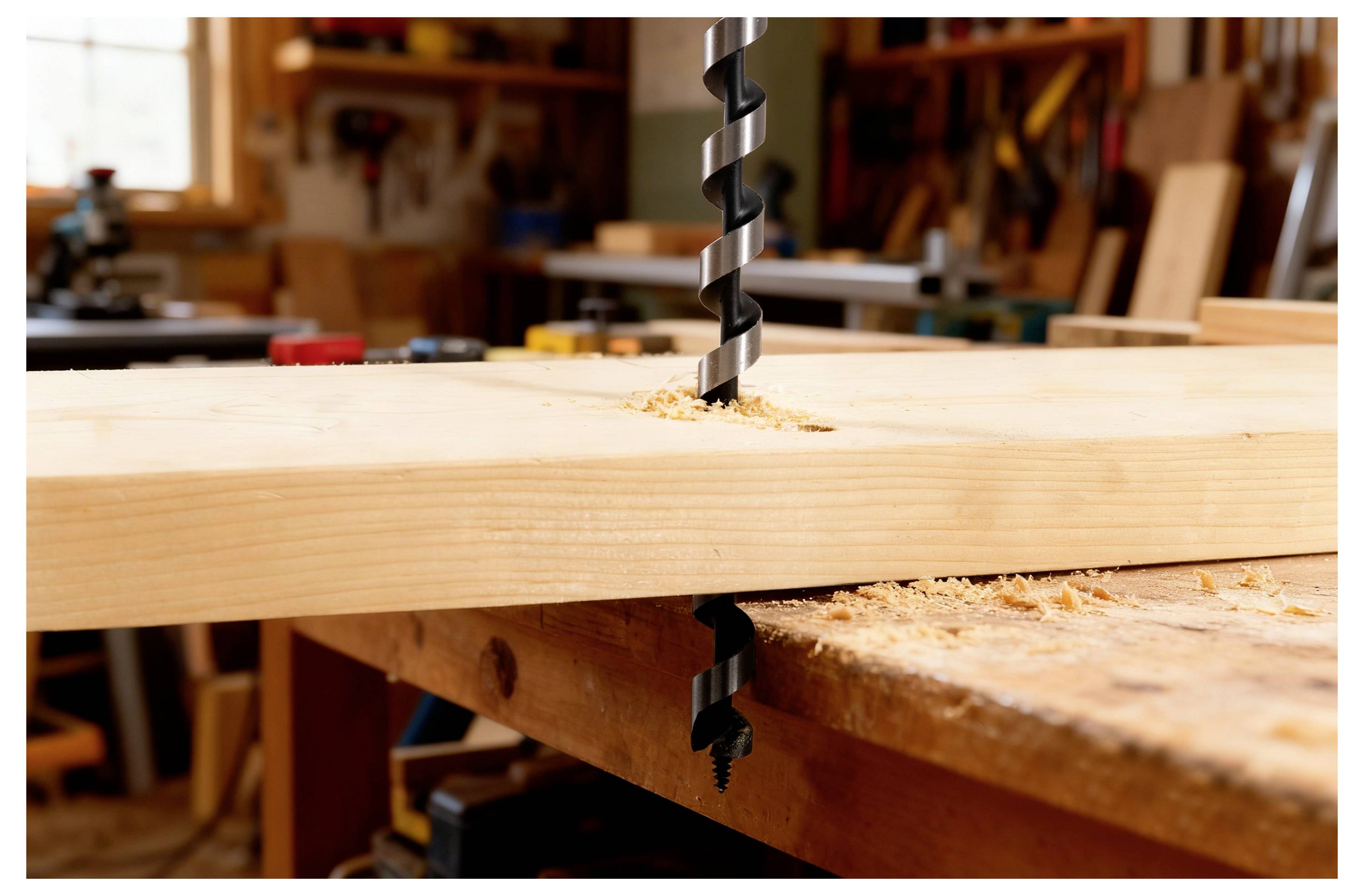 Eine Bohrmaschine bohrt durch eine Holzplanke auf einer Werkbank, mit Holzspänen, die umhergestreut sind und einen Moment der Holzbearbeitung einfangen.