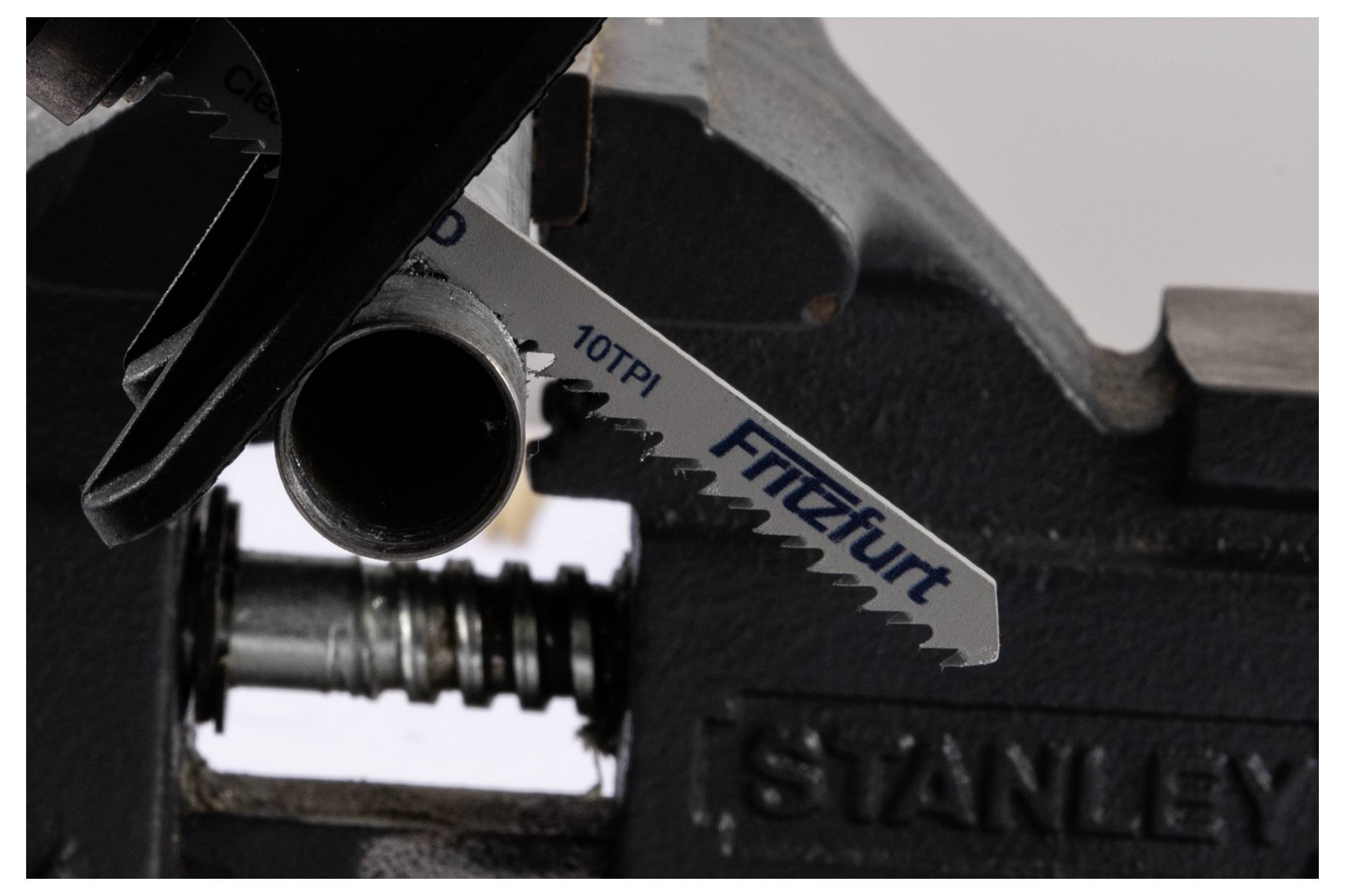 Eine Sägeblatt mit der Bezeichnung FITZALL 10TPI, eingespannt in eine Vise-Grip-Zange der Marke STANLEY, positioniert zum Schneiden eines Metallrohrs.