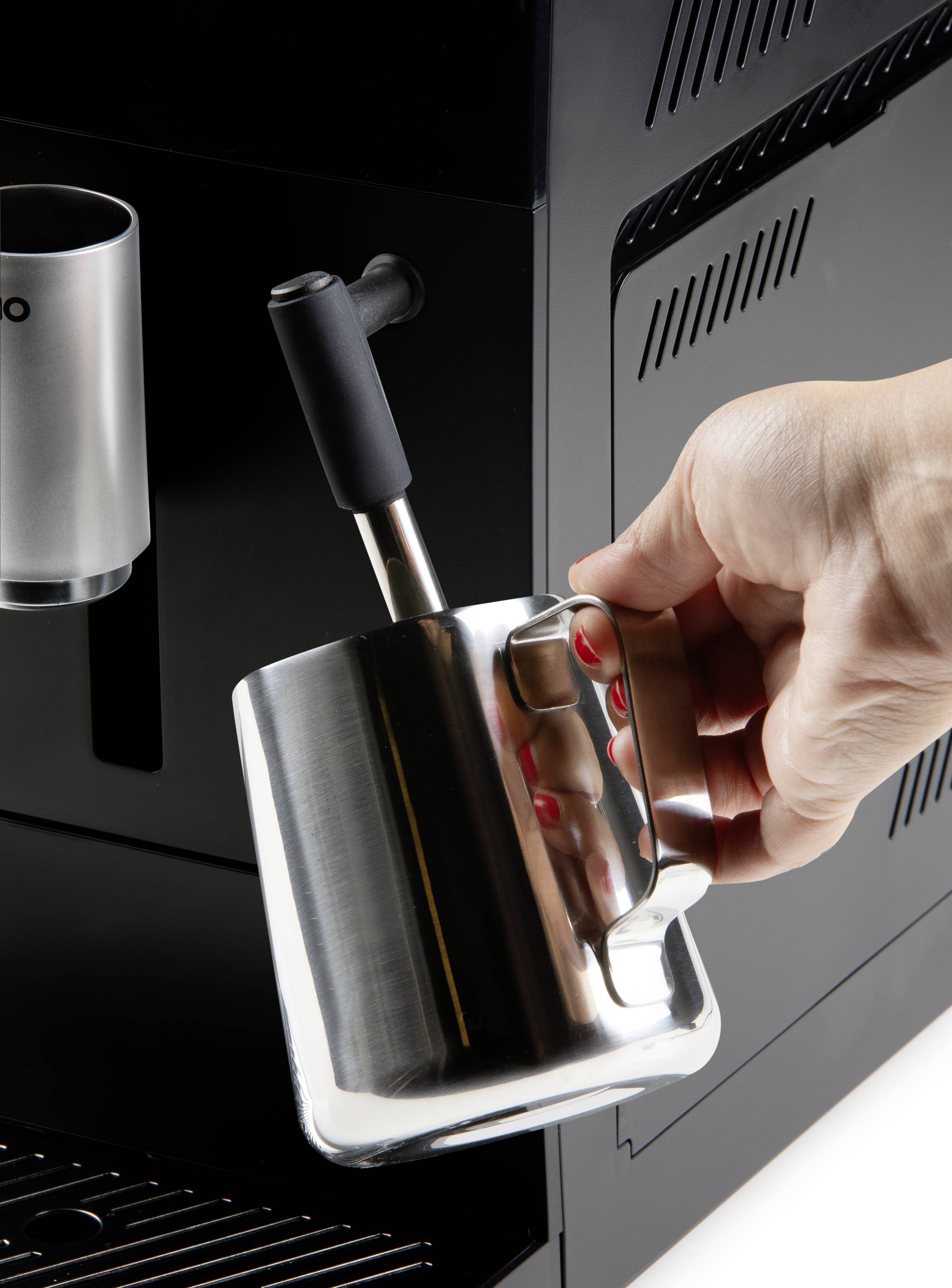 Eine Hand hält einen Edelstahl-Milchkrug unter einer Dampfdüse einer Kaffeemaschine, bereit zum Aufschäumen der Milch.