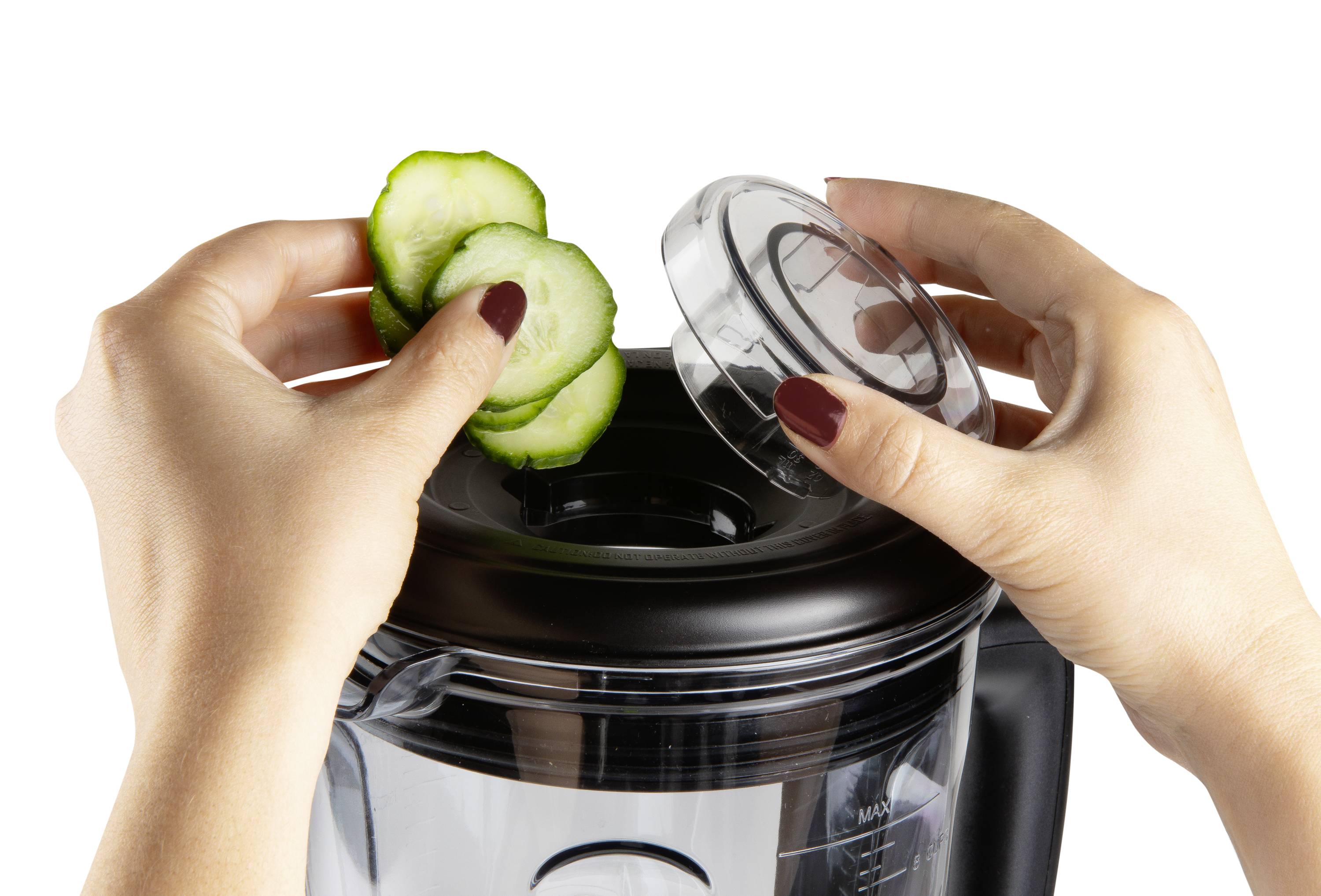 Eine Person legt Gurkenscheiben in einen Mixer, dessen Deckel in der anderen Hand gehalten wird.
