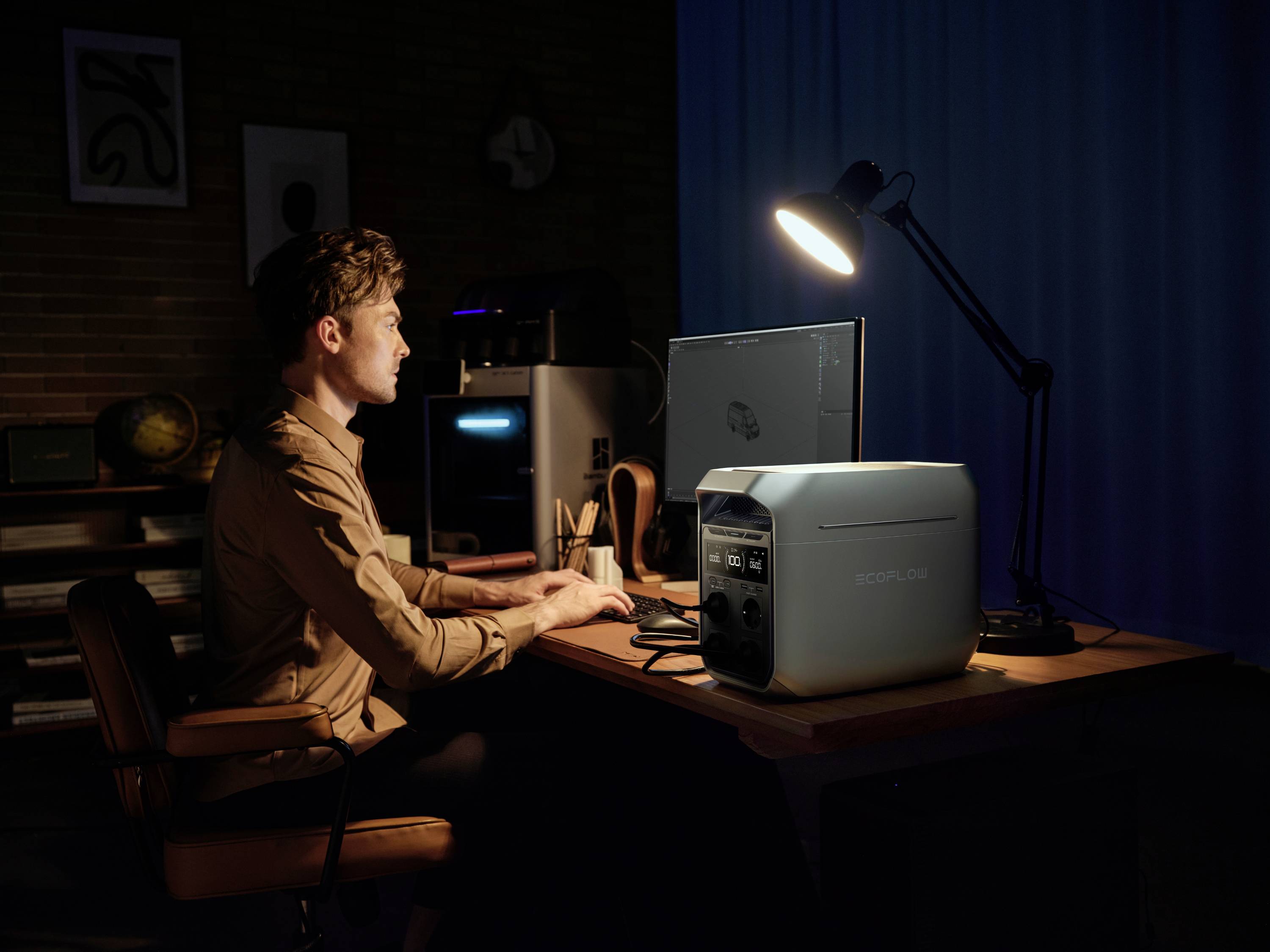 Eine Person sitzt in einem dunklen Raum am Schreibtisch, arbeitet am Computer mit einer Lampe und einem tragbaren Generator auf dem Tisch.