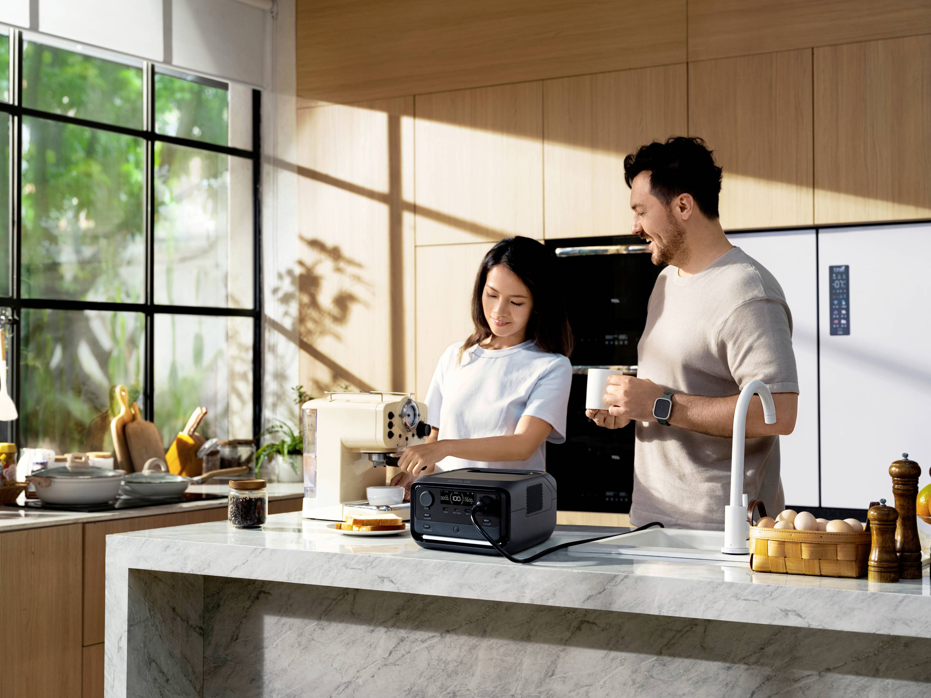 Eine Frau bereitet Kaffee an einer Maschine zu, während ein Mann daneben steht und eine Tasse hält. Beide befinden sich in einer modernen Küche.