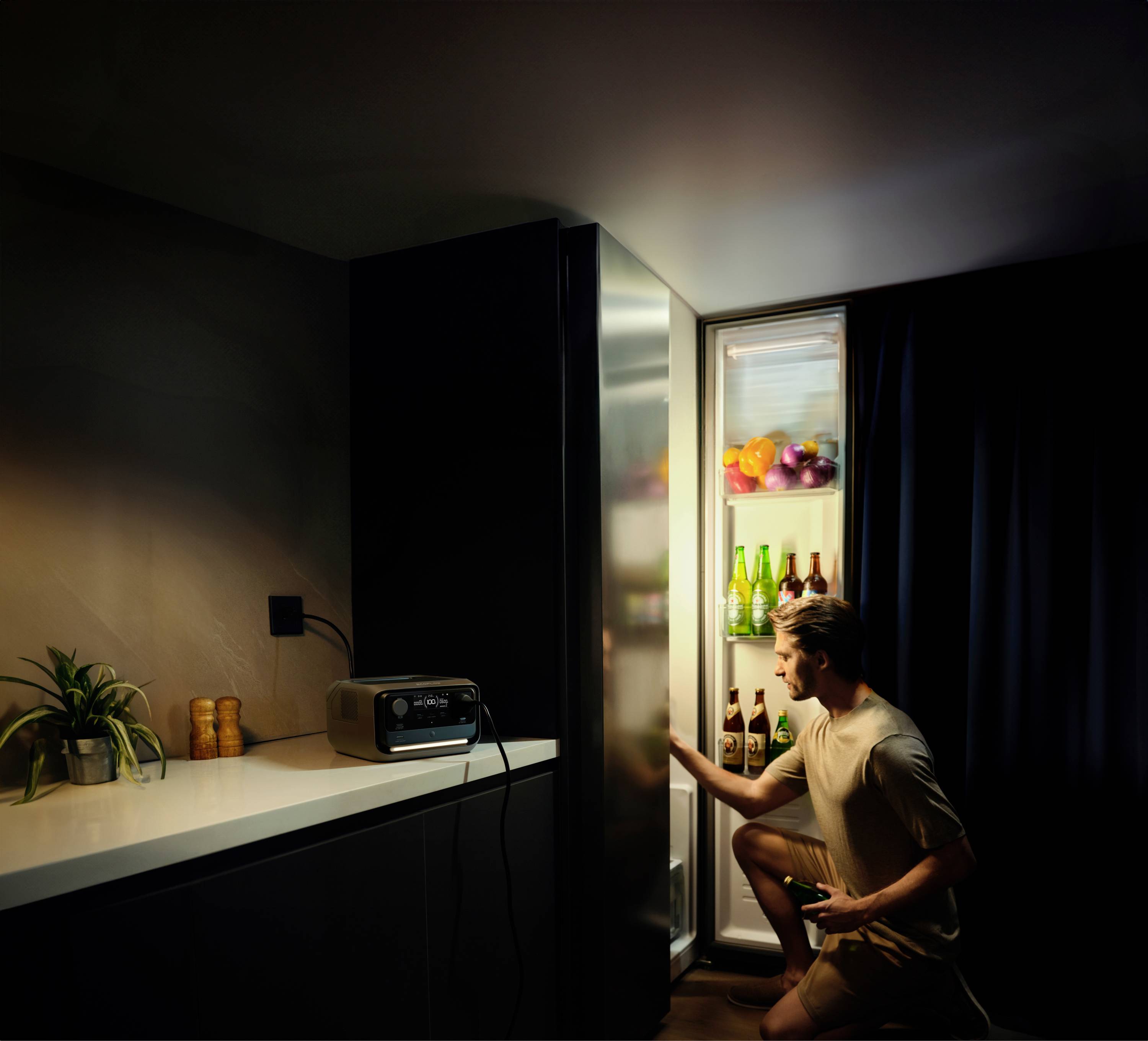 Ein Mann öffnet einen beleuchteten Kühlschrank in einer dunklen Küche, hält ein Getränk und betrachtet den Inhalt.
