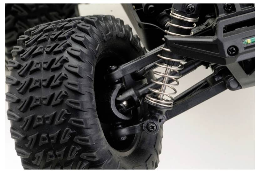 Nahaufnahme des Rades eines Geländefahrzeugs mit großem Profilreifen und sichtbaren Federungsfedern, was die Fähigkeit für raues Gelände anzeigt.