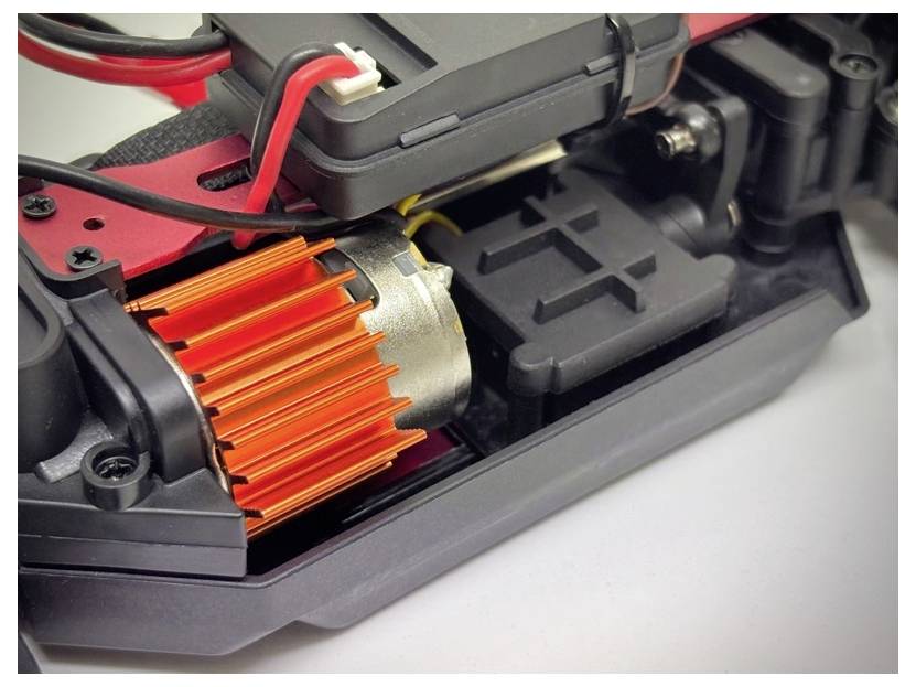 Nahaufnahme eines kleinen Elektromotors mit einem orangefarbenen Kühlkörper, der in einer schwarzen und roten mechanischen Baugruppe montiert ist, wahrscheinlich für ein ferngesteuertes Fahrzeug.