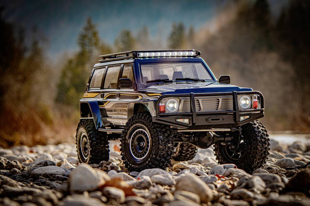 Ein schwarzes Offroad-Spielzeugauto steht auf einem steinigen Gelände, umgeben von Bäumen und Bergen im Hintergrund.