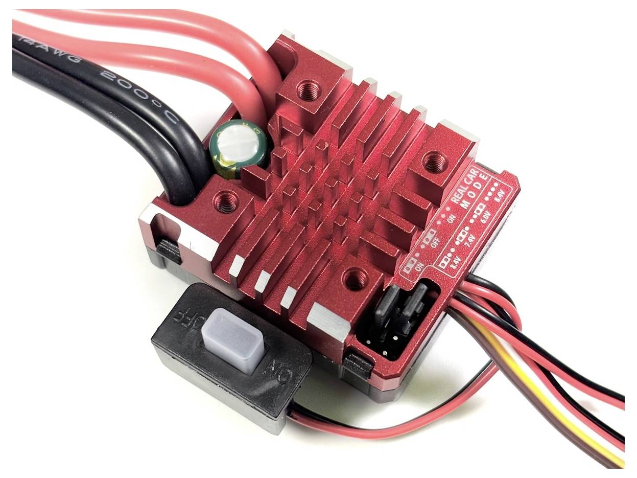 Ein roter elektrischer Regler mit Kühlrippen, mehreren Kabelanschlüssen und einem schwarzen Kippschalter, dient zur Steuerung von Motoren.