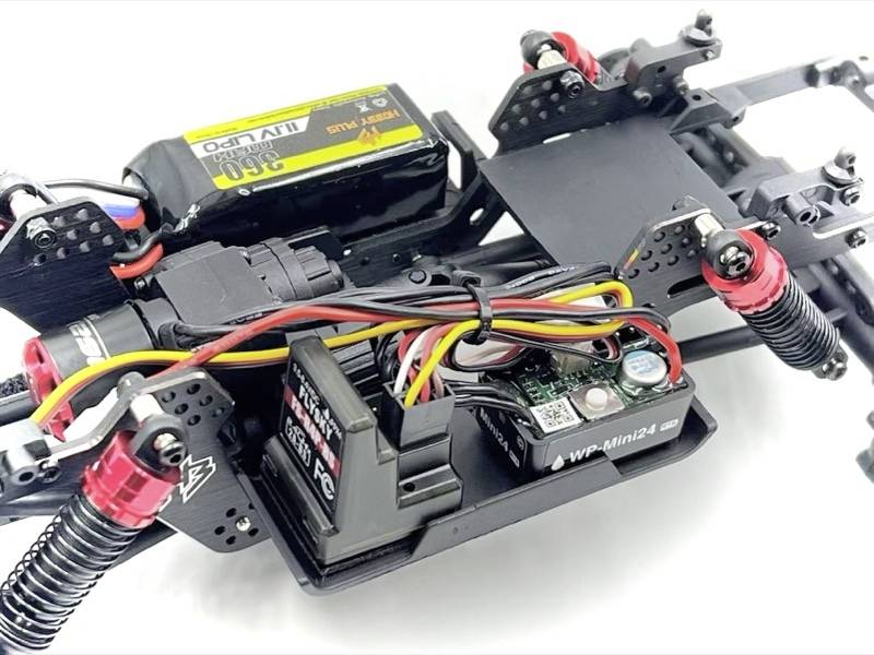 Nahaufnahme eines ferngesteuerten Autorahmens mit Elektronik und Verkabelung, inklusive Batterie und Stoßdämpfer.