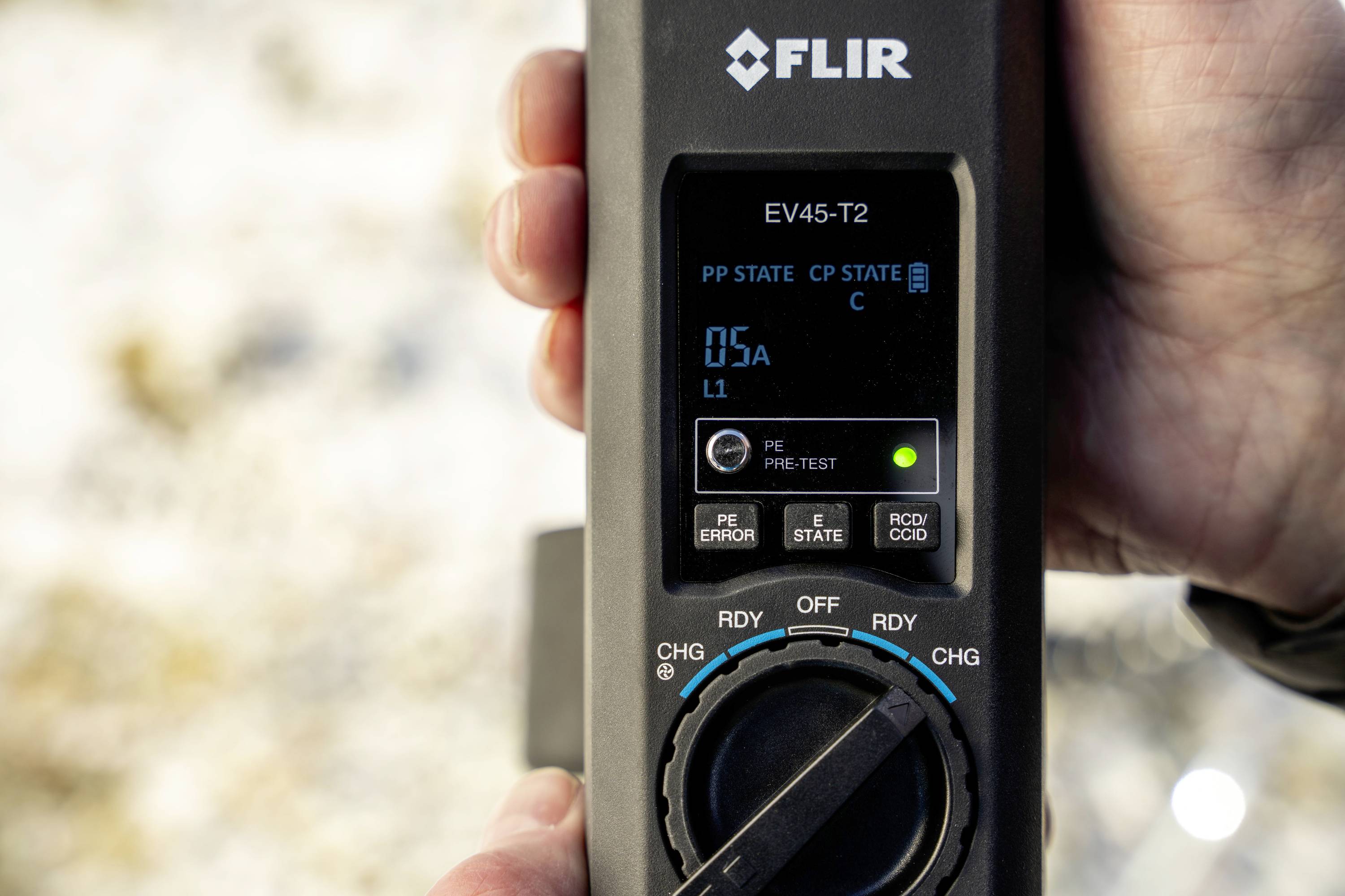 Eine Hand hält ein FLIR EV45-T2 Gerät, das 0,5A anzeigt. Das Display zeigt Statusinformationen und verschiedene Betriebsmodi.