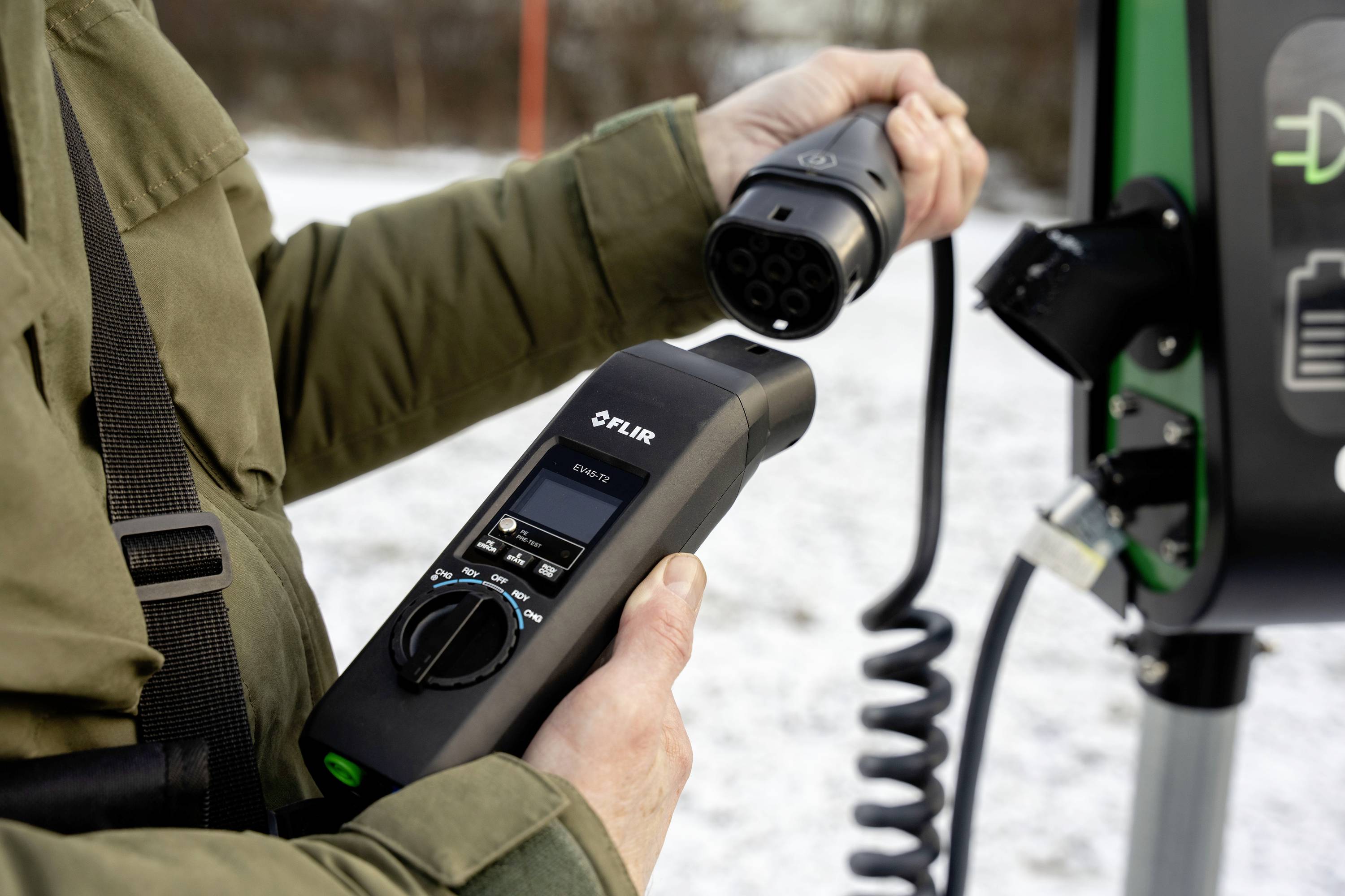 Person lädt ein Elektroauto an einer Ladestation auf. Er hält ein Ladekabel in der Hand und schließt es an die Station an.