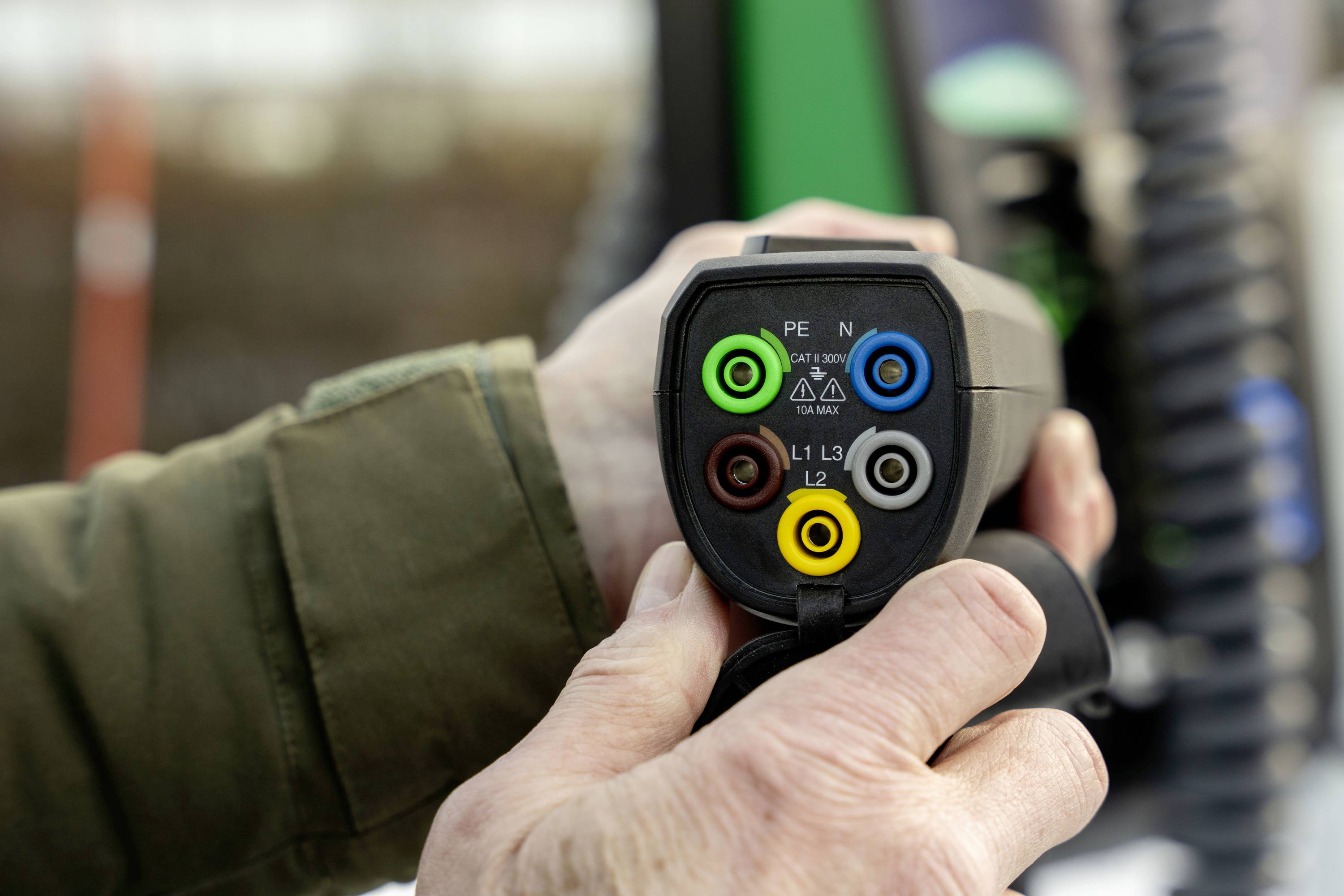 Person hält ein Stecker mit farbigen Anschlussbuchsen: grün, blau, braun, gelb, schwarz. Möglicherweise für Elektrofahrzeuge.