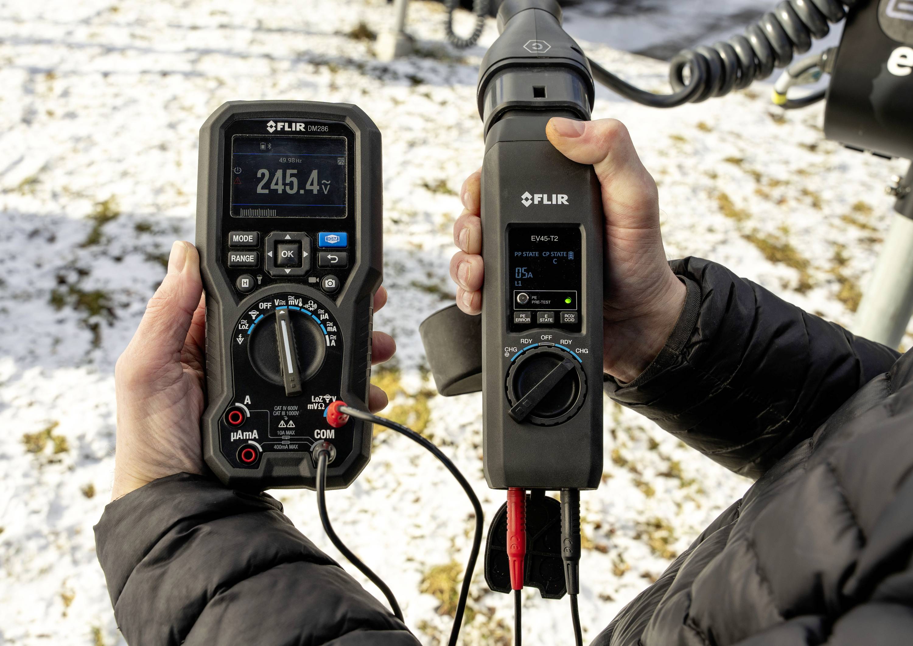 Person hält FLIR-Messgeräte im Freien. Das linke Display zeigt 245,4V, das rechte zeigt 0,0 Lux.