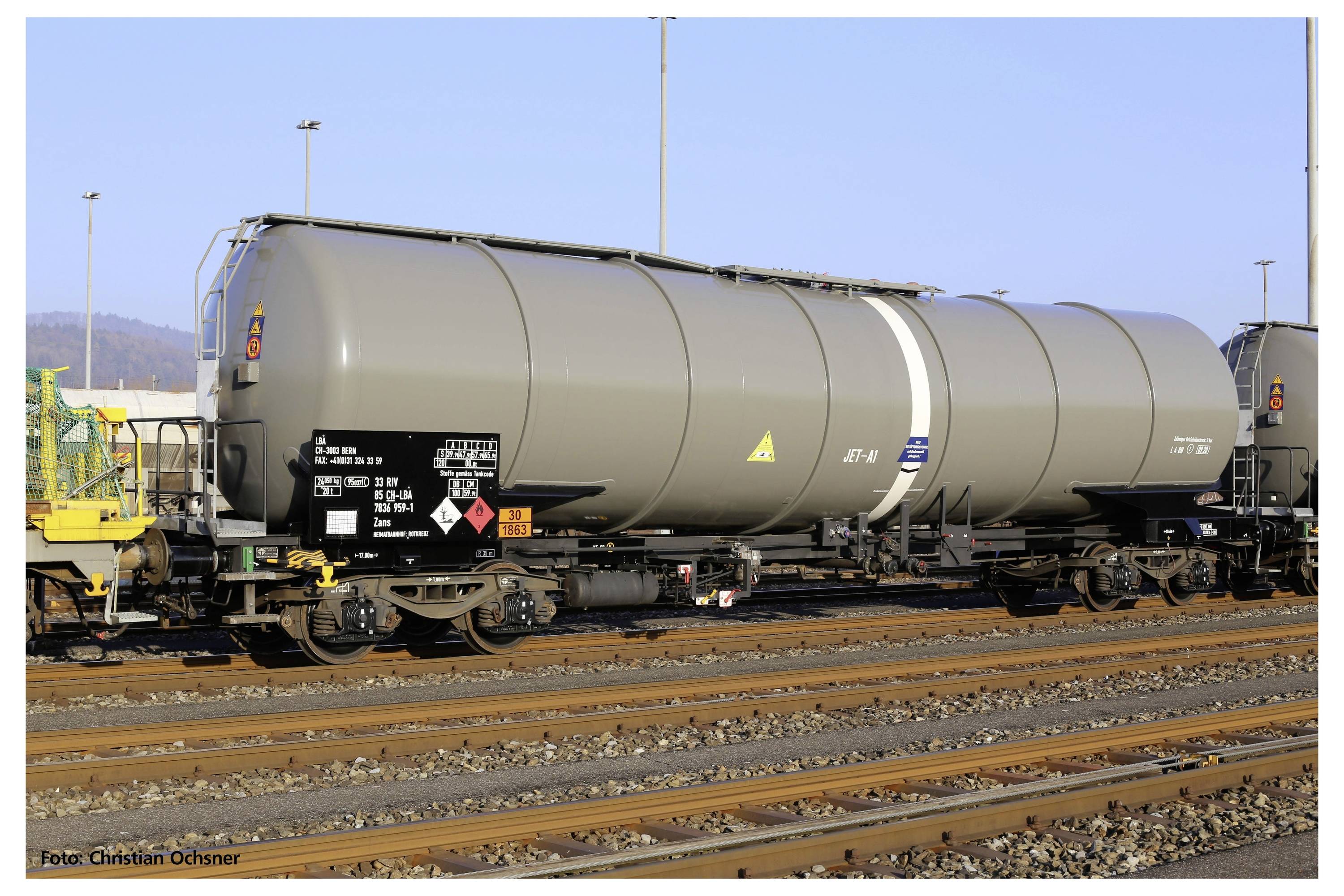 Ein Kesselwagen auf Bahngleisen mit Warnsymbolen und technischen Markierungen, fotografiert bei Tageslicht auf einem Güterbahnhof.