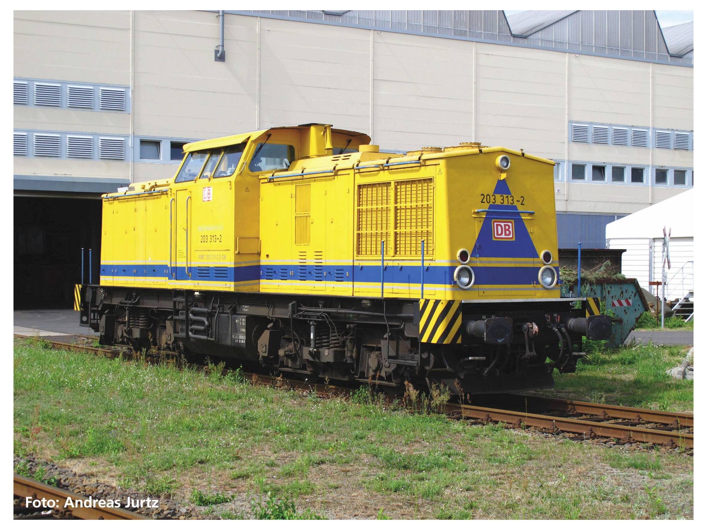 Eine gelb-blaue Lokomotive steht auf einem Gleis vor einem großen Gebäude.