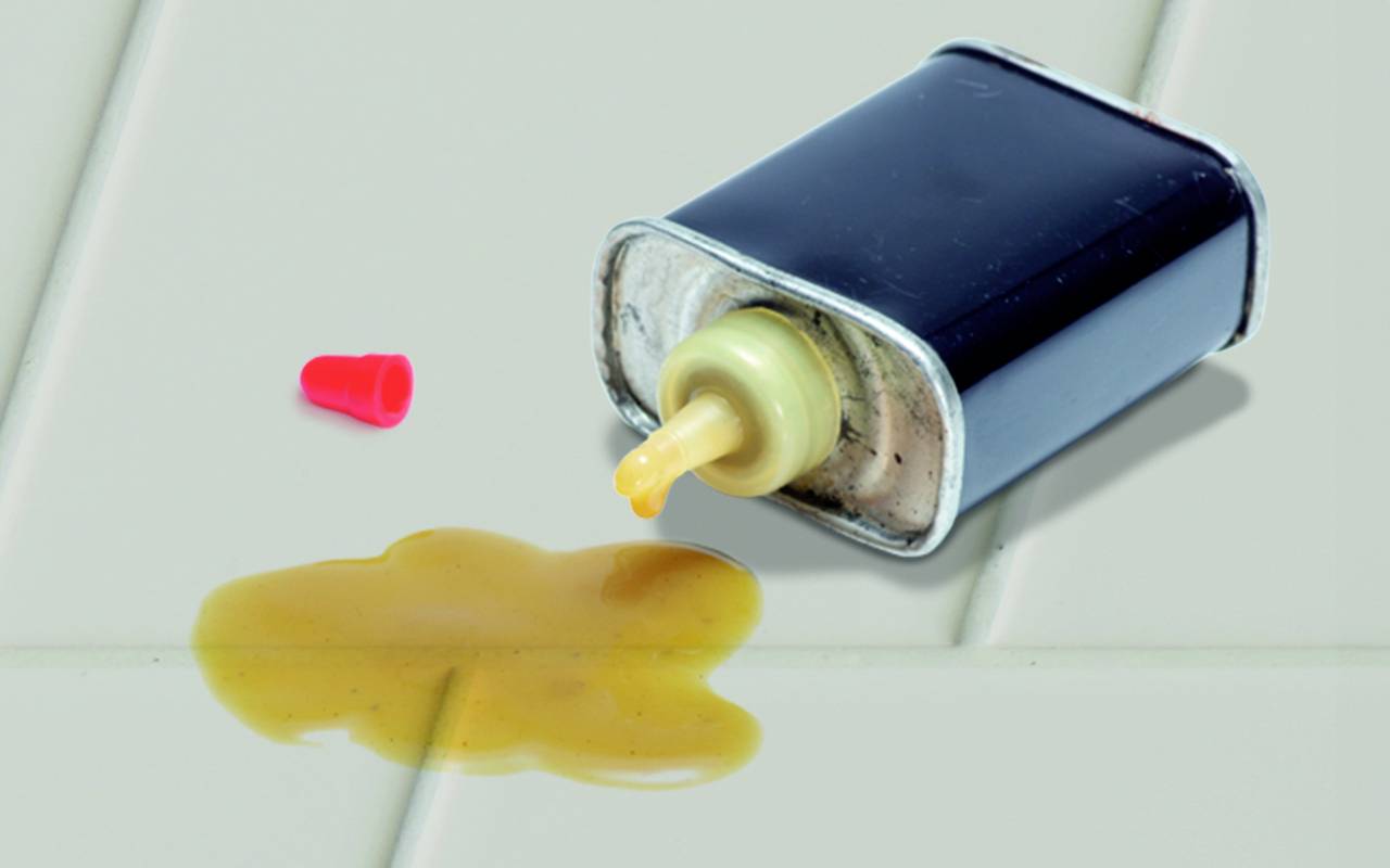 Eine umgefallene Dose mit verschüttetem gelbem Flüssigkleber auf einem Tisch. Ein roter Verschluss liegt daneben.