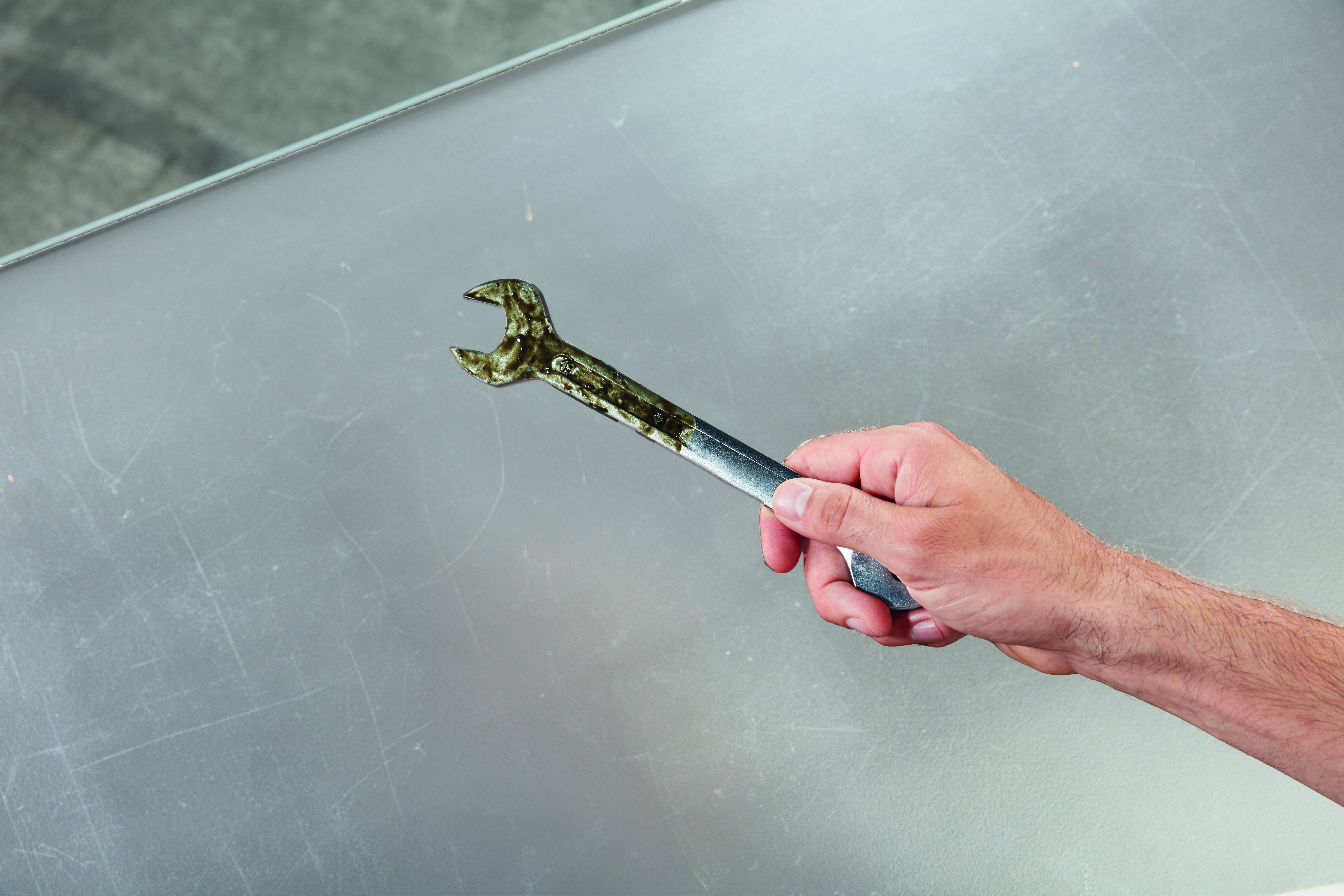 Eine Hand hält einen Schraubenschlüssel gegen eine große zerkratzte Metalloberfläche.