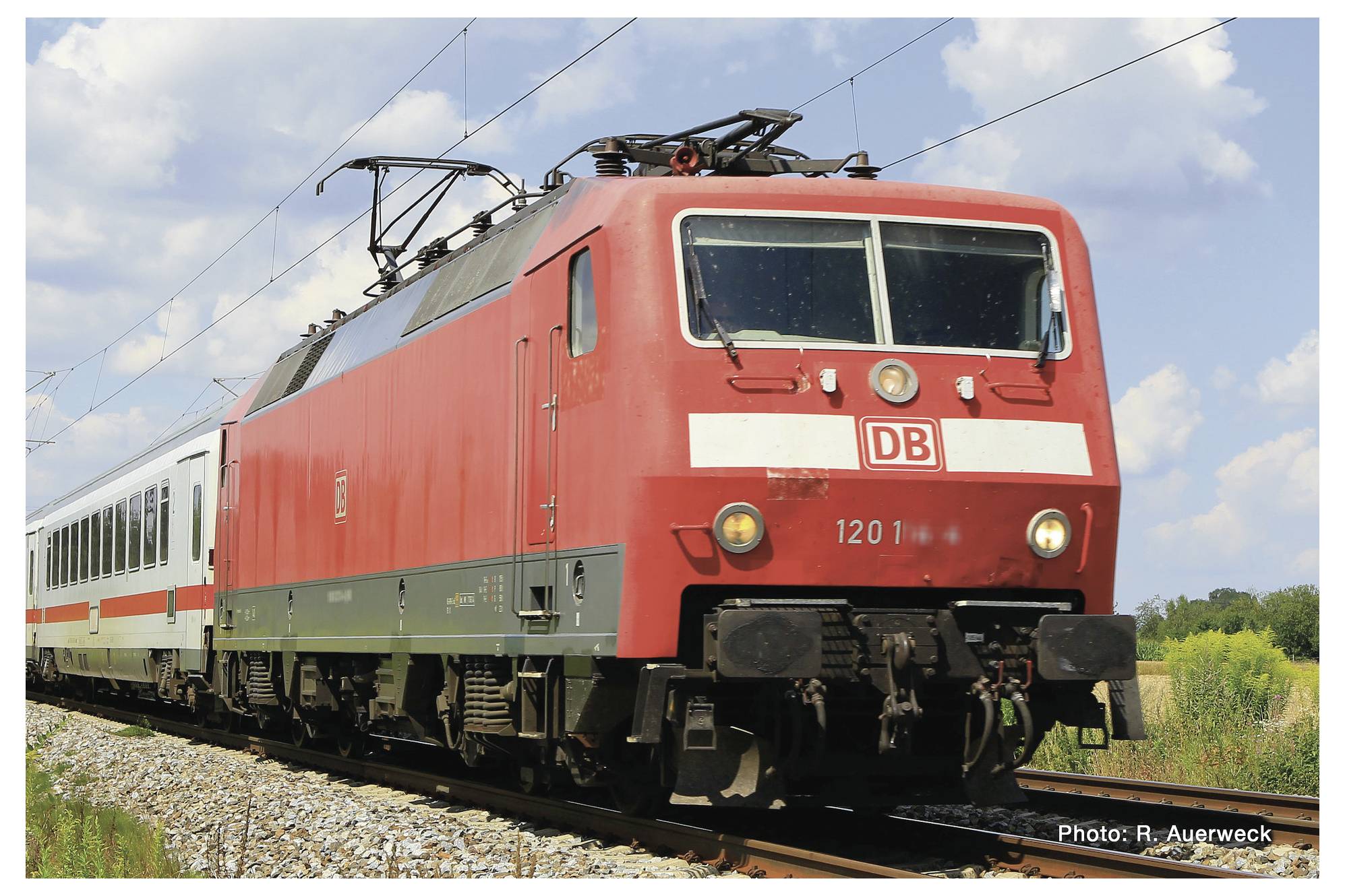 Ein roter Intercity-Zug der Deutschen Bahn fährt auf einem Gleis durch eine ländliche Landschaft. Der Himmel ist klar und sonnig.