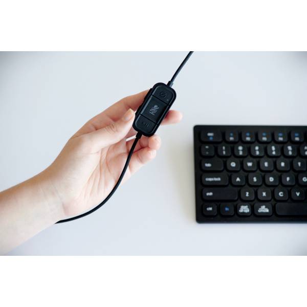 Eine Hand hält eine Kabelsteuerung mit Lautstärkeregler neben einer Tastatur.