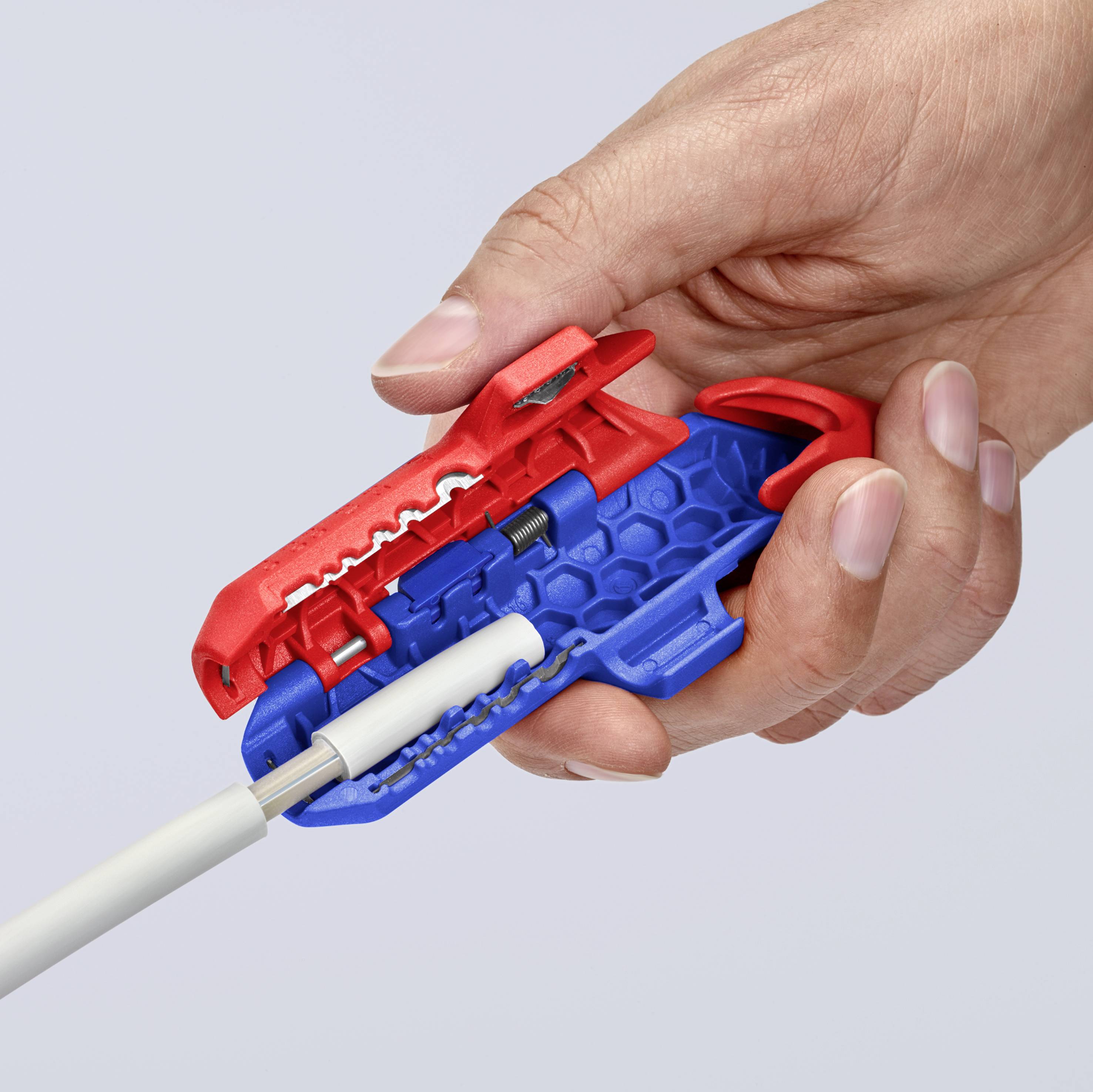Eine Hand hält ein rotes Tool, das ein Kabel abisoliert. Das Werkzeug zieht die Ummantelung ab, um das innere Kabel freizulegen.