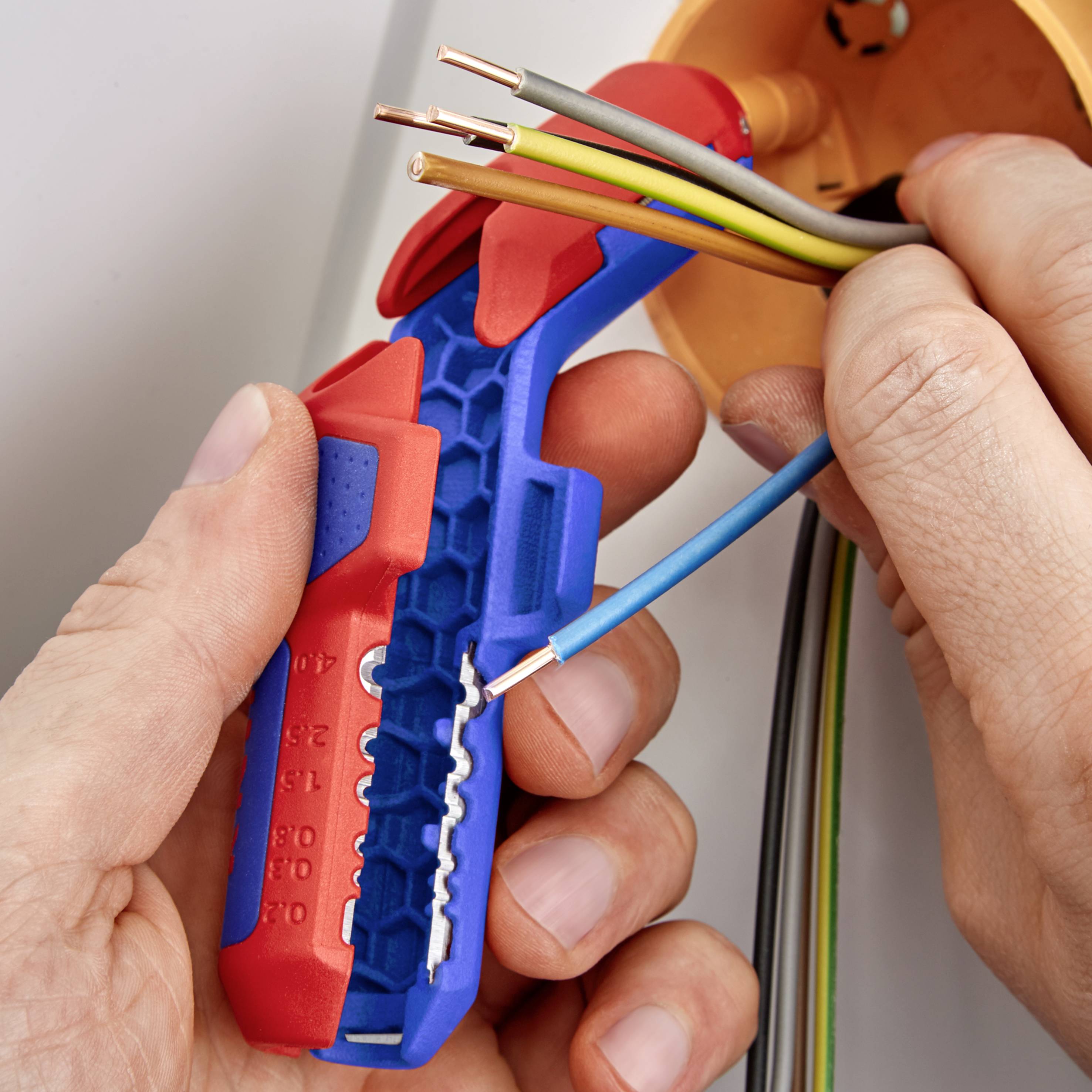Eine Person verwendet ein Abisolierwerkzeug, um die Enden mehrerer elektrischer Kabel freizulegen.