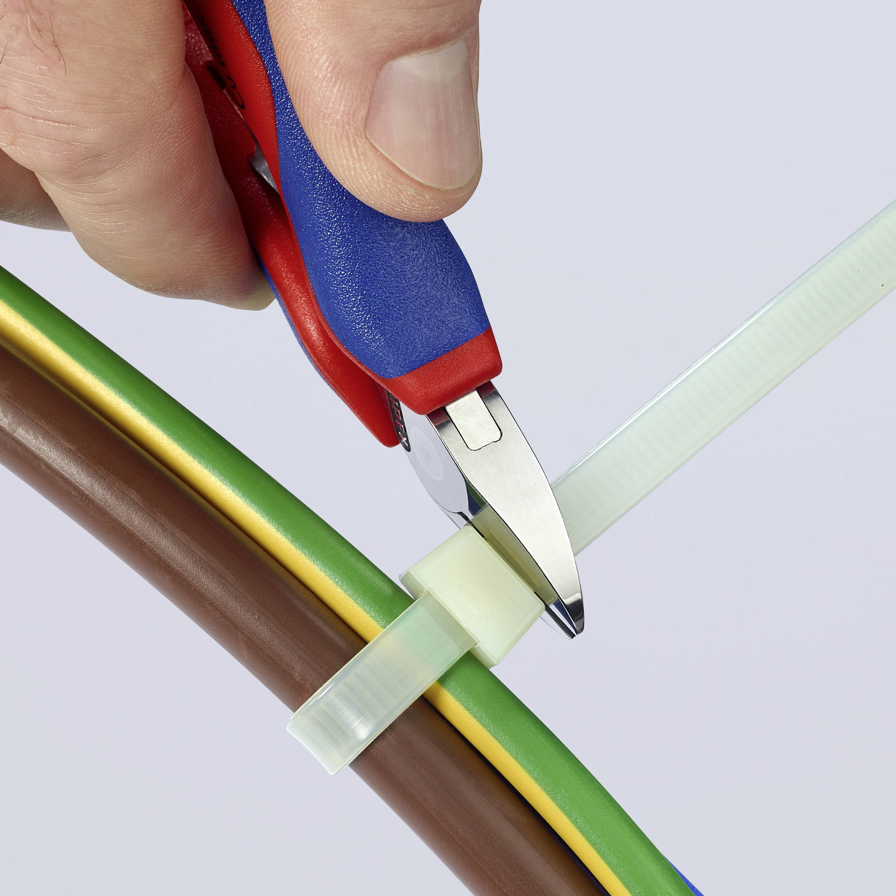 Eine Hand hält einen Seitenschneider und schneidet einen Kabelbinder, der mehrere bunte Kabel zusammenhält.