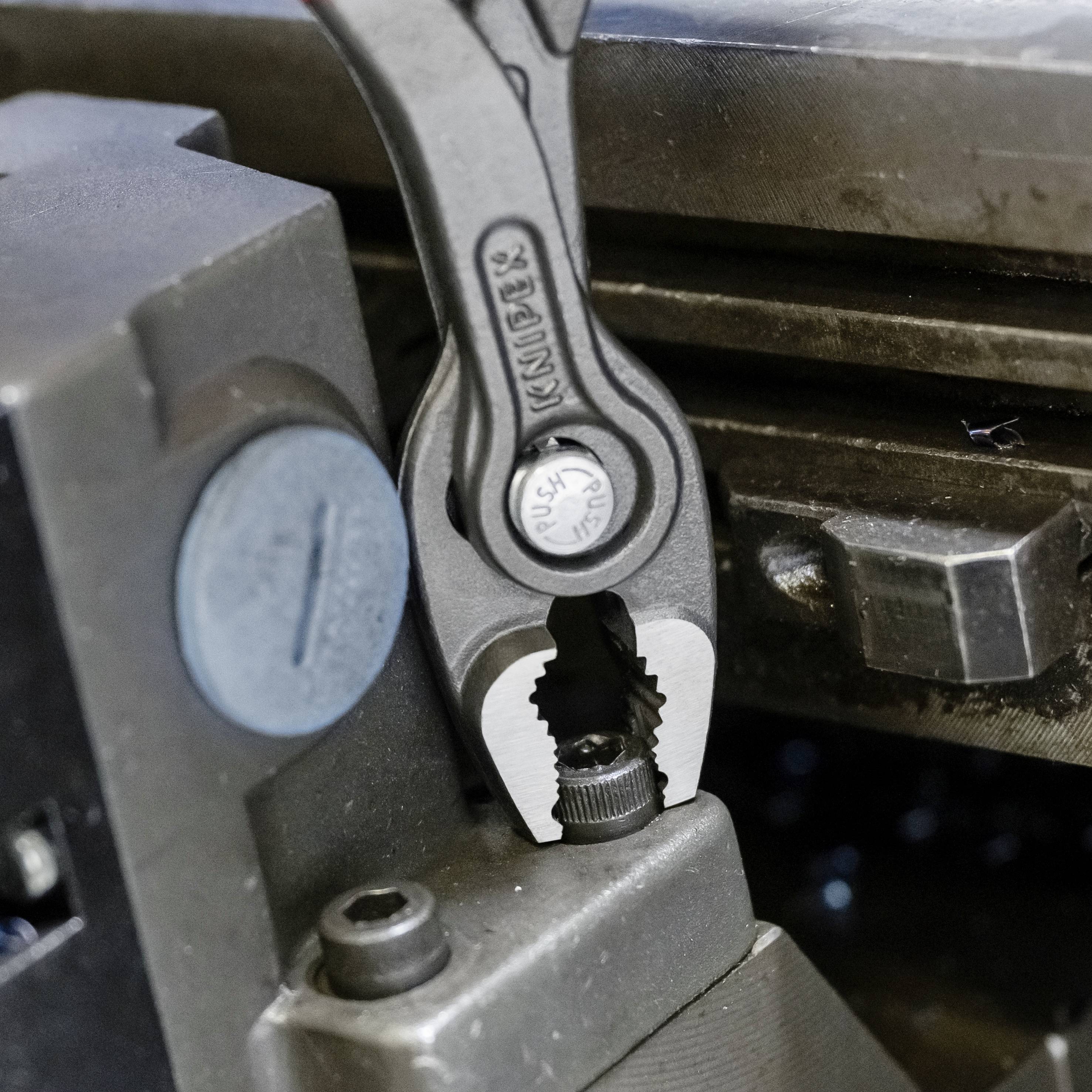 Eine Zange greift ein Metallteil in einer Werkstattumgebung. Sie befindet sich in einer Klemme und wird bearbeitet oder eingestellt.