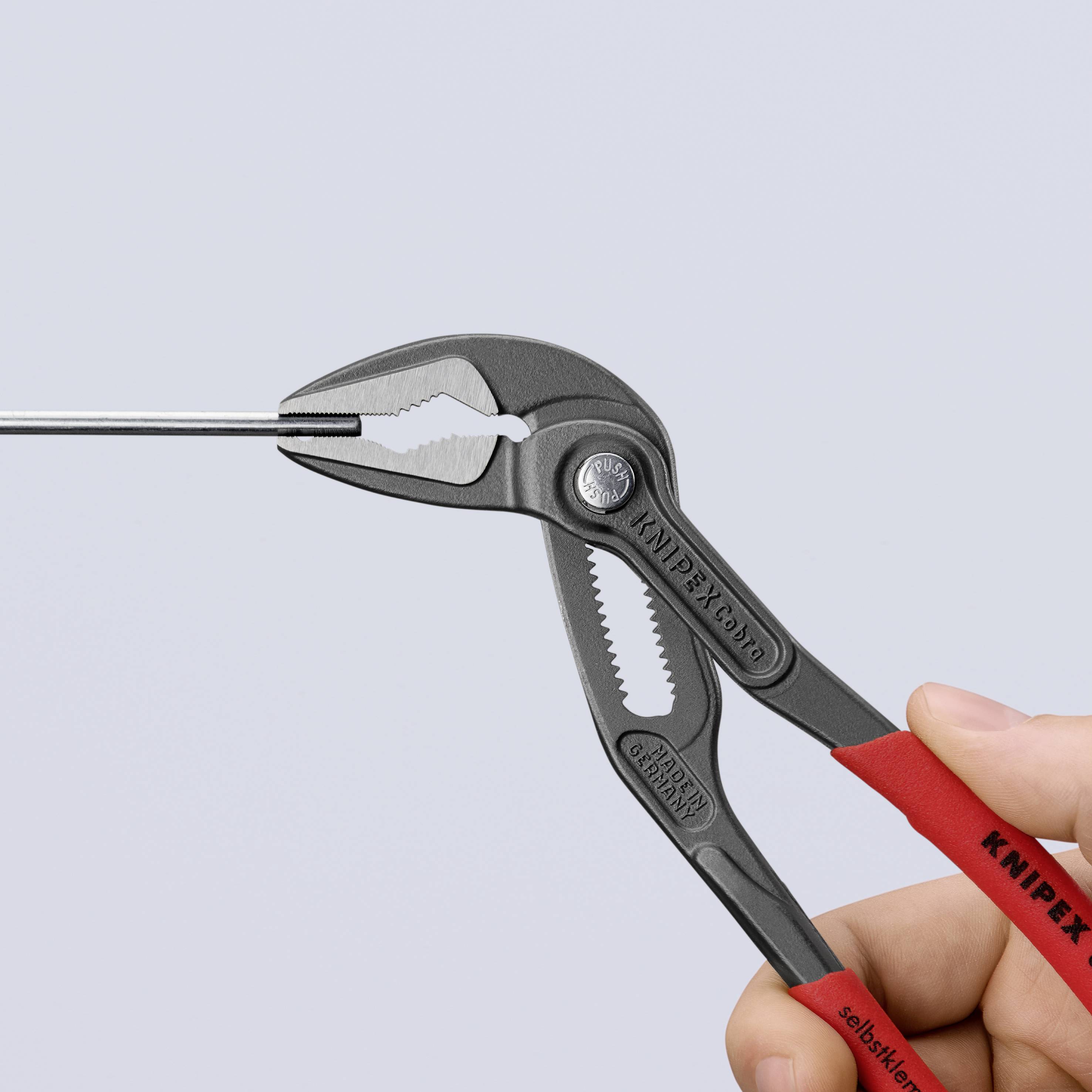 Eine Hand hält eine graue Knipex-Wasserpumpenzange mit rotem Griff und spannt einen Metallstab ein.