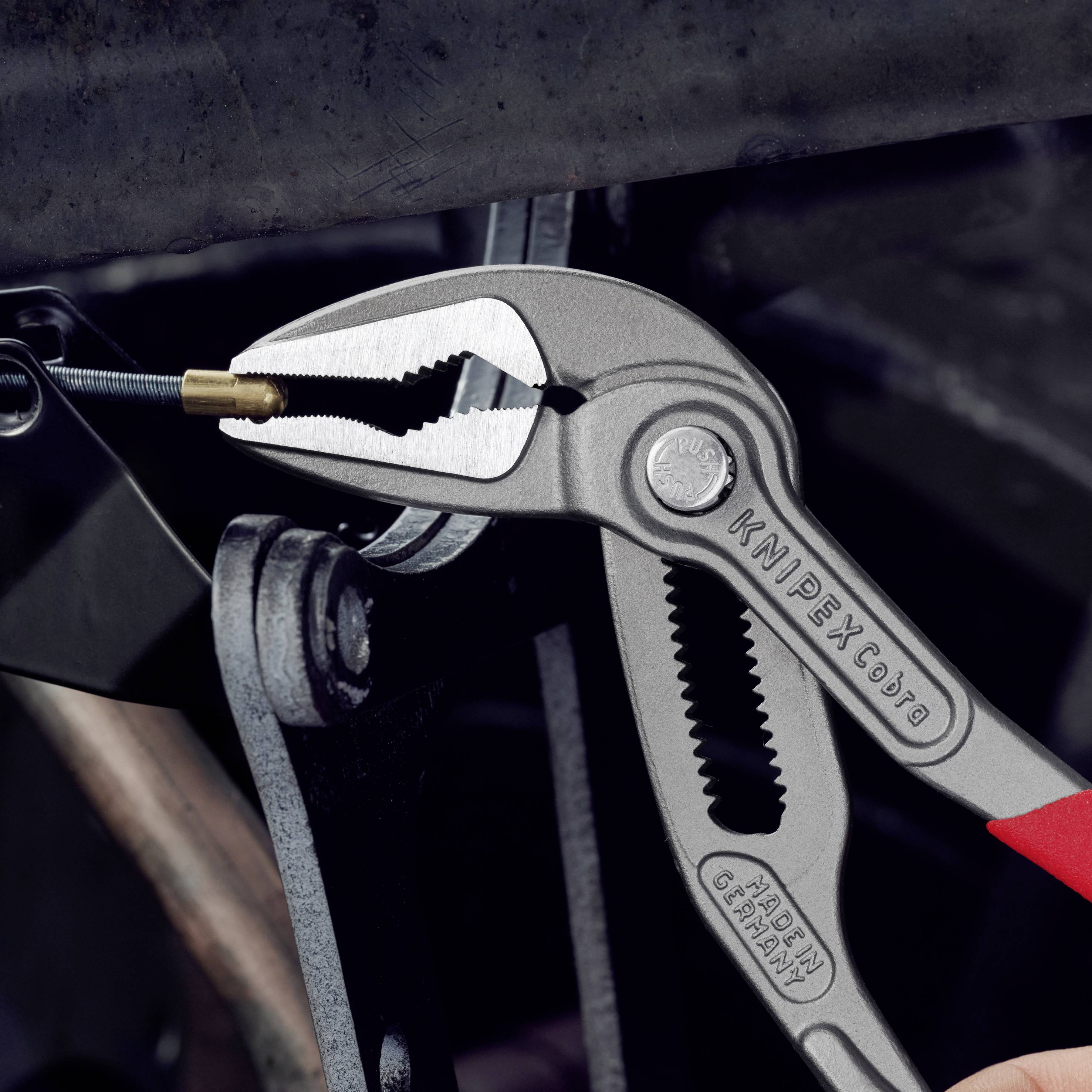 Eine Hand hält eine silberne Zange mit rotem Griff, die eine kleine Schraube festhält. Die Zange hat die Aufschrift 'KNIPEX'.