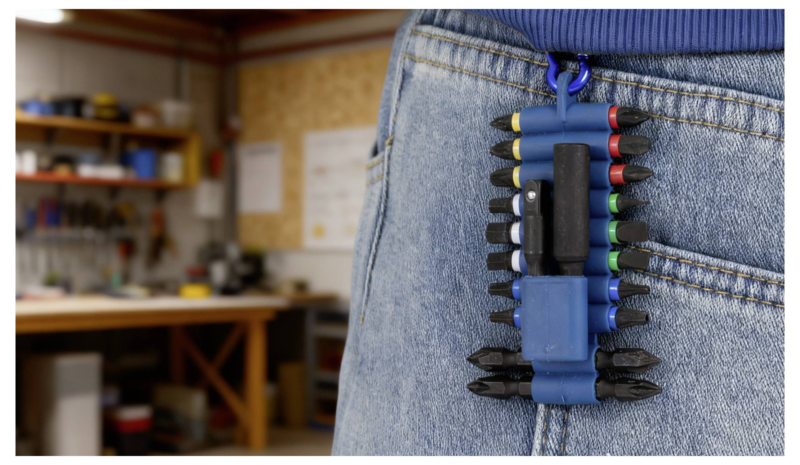 Ein Mehrbit-Schraubendreher mit einem blauen Halter, der an der Gesäßtasche einer Jeans befestigt ist und verschiedene farbige Bits zeigt. Eine Werkstatt ist im Hintergrund unscharf.
