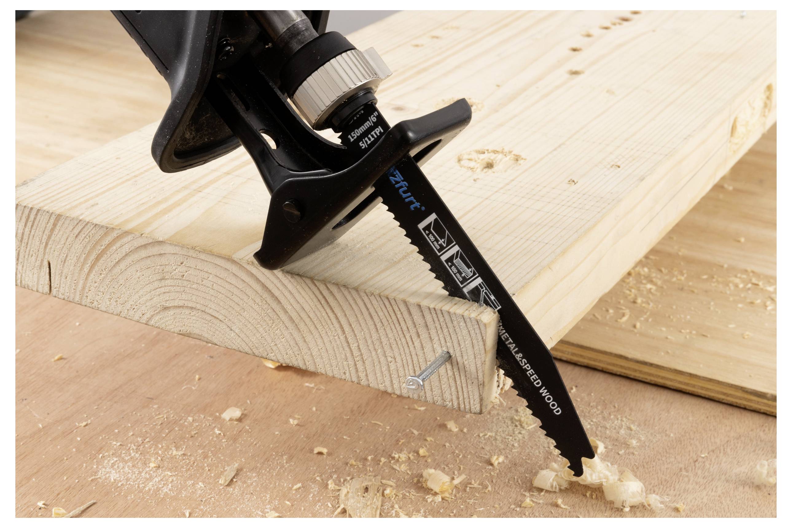 Eine Sägeblatt, das durch ein Holzbrett schneidet und Holzspäne hinterlässt. Das Brett ist durch eine Schraube befestigt. Das Sägeblatt ist mit Spezifikationen beschriftet.