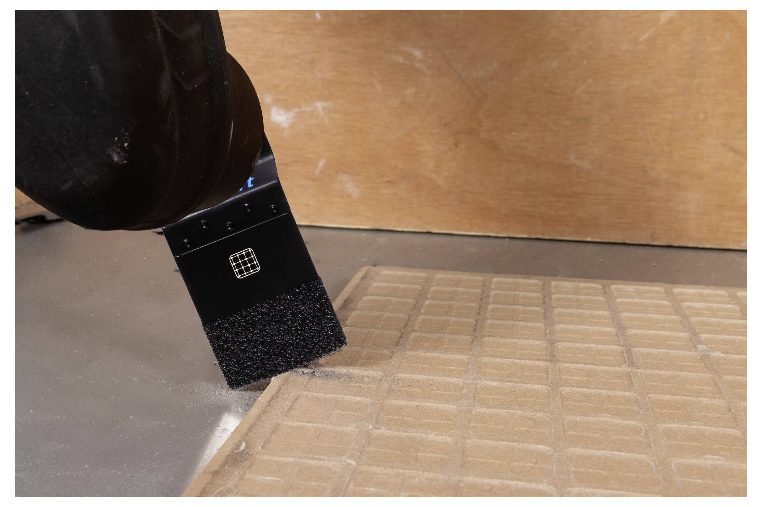 Ein Staubsaugerroboter mit Bürstenaufsatz, der Staub von einer strukturierten Matte auf einem Holzboden reinigt.