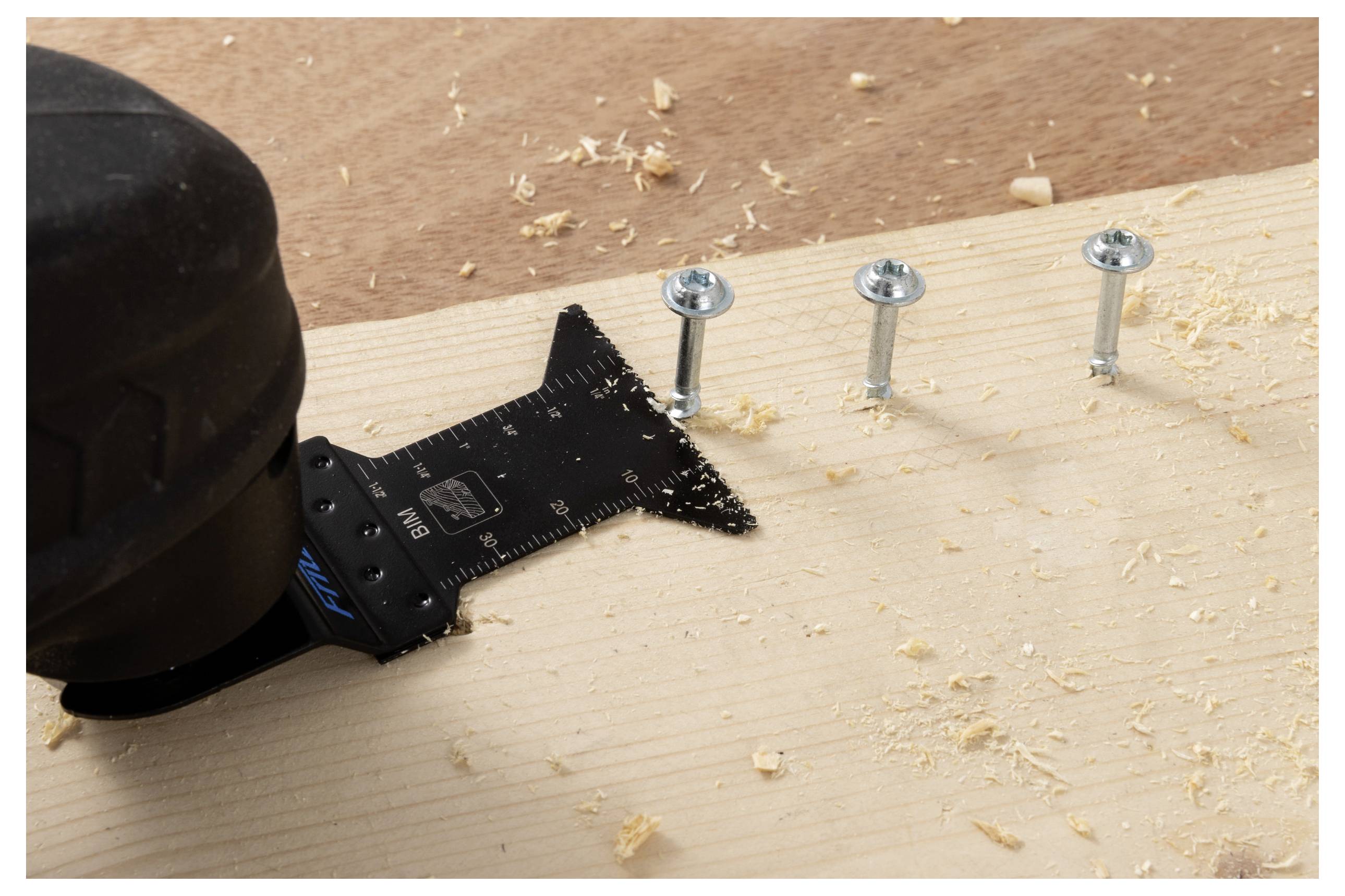 Eine Elektrowerkzeug mit einer Multifunktionsklinge schneidet in Holz nahe drei Schrauben, umgeben von Holzspänen auf einer Holzoberfläche.