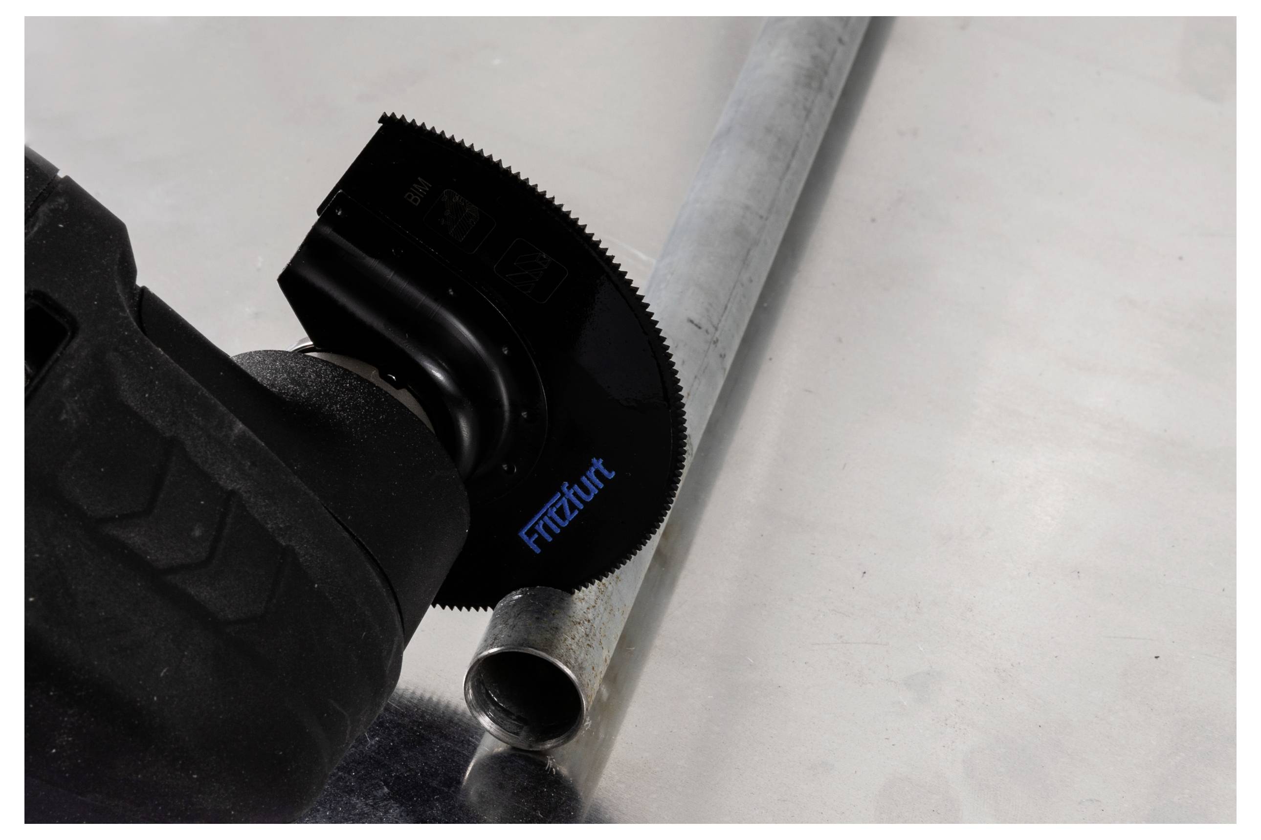 Eine Elektrowerkzeug mit einer kreisförmigen Säge schneidet ein Metallrohr. Auf der Klinge ist das Wort 'Friedfurt' gedruckt.