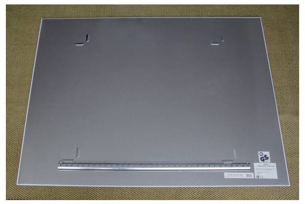 Metalplatte mit eingedrückten Ecken auf einer Holzoberfläche. Eine Metallschiene mit Linealmarkierungen ist am unteren Rand befestigt.