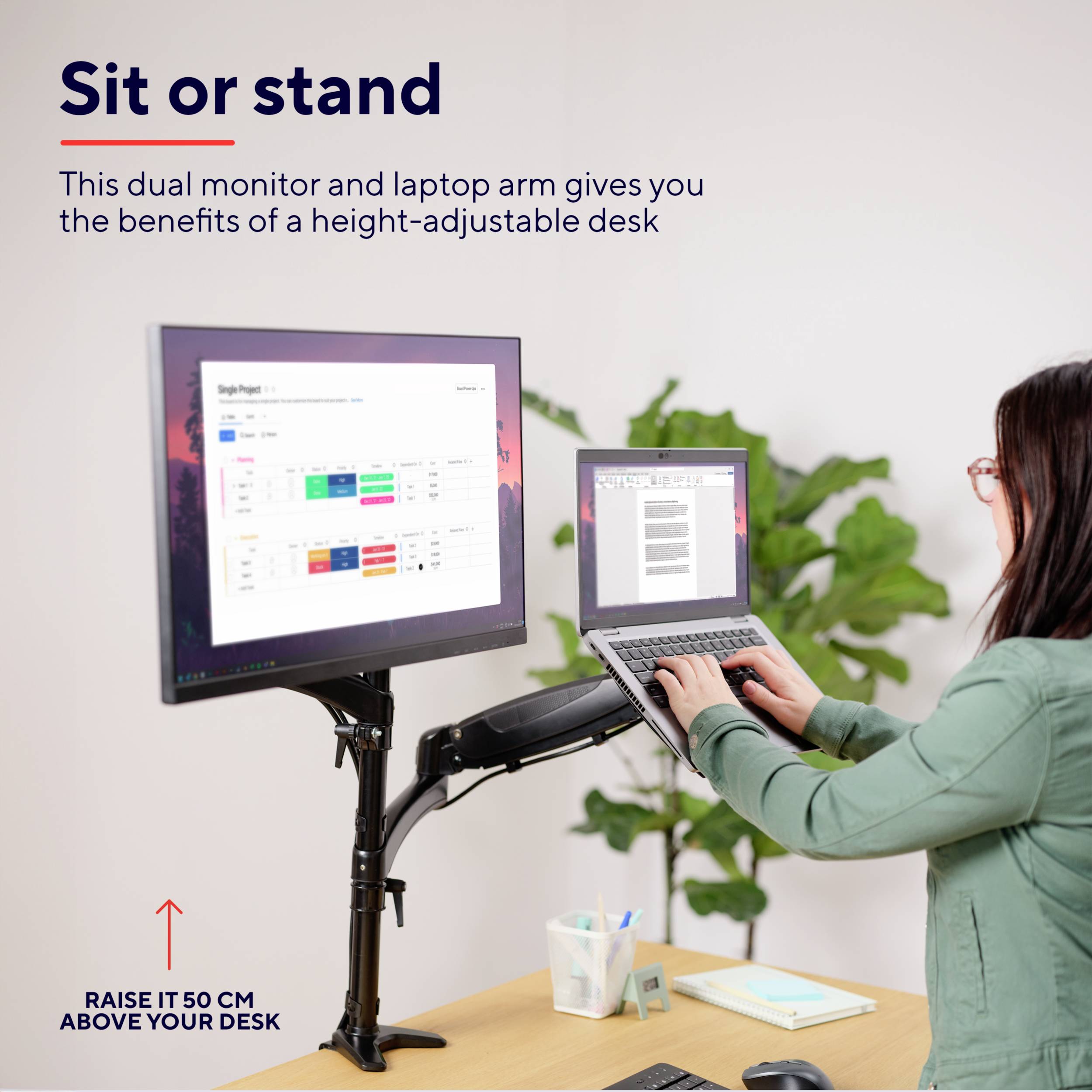 Eine Person arbeitet an einem Laptop, der auf einem höhenverstellbaren Schreibtisch mit zwei Monitoren montiert ist. Text: 'Sit or stand'.