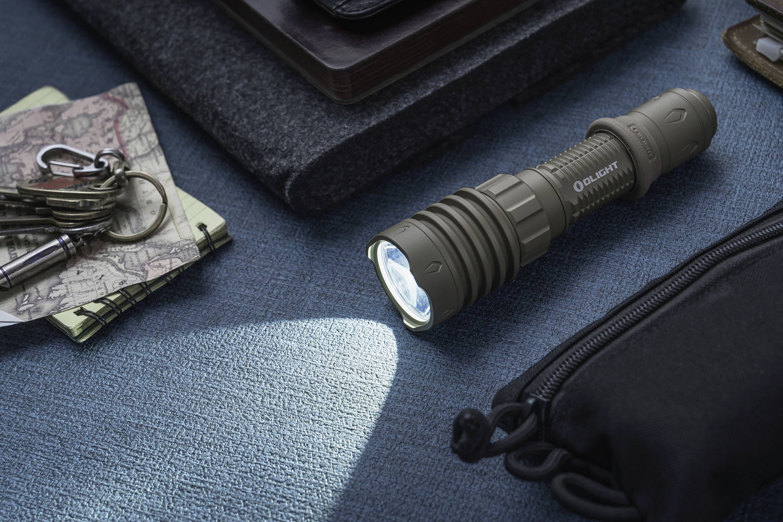 Taschenlampe liegt auf blauem Stoff, leuchtet, umgeben von Schlüssel, Karte, und Tasche.