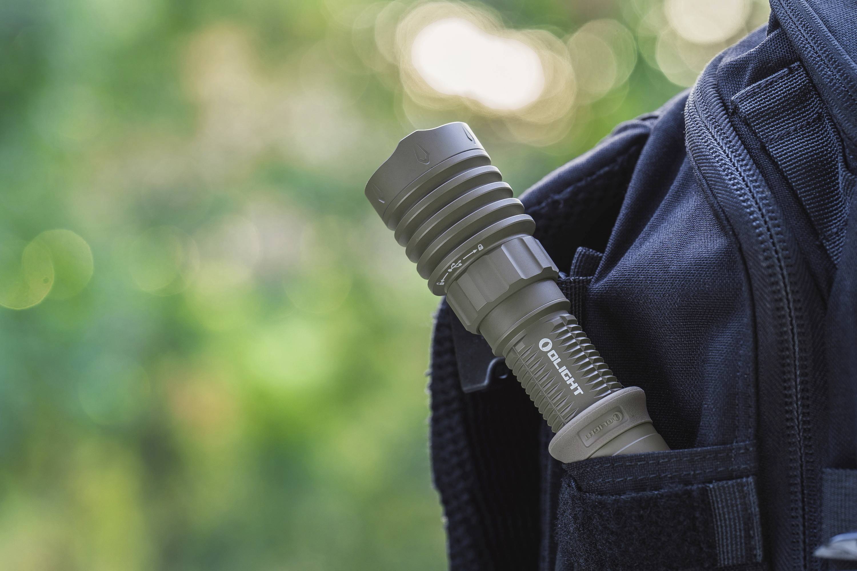 Eine Taschenlampe steckt in der Seitentasche eines Rucksacks, vor einem verschwommenen Hintergrund.