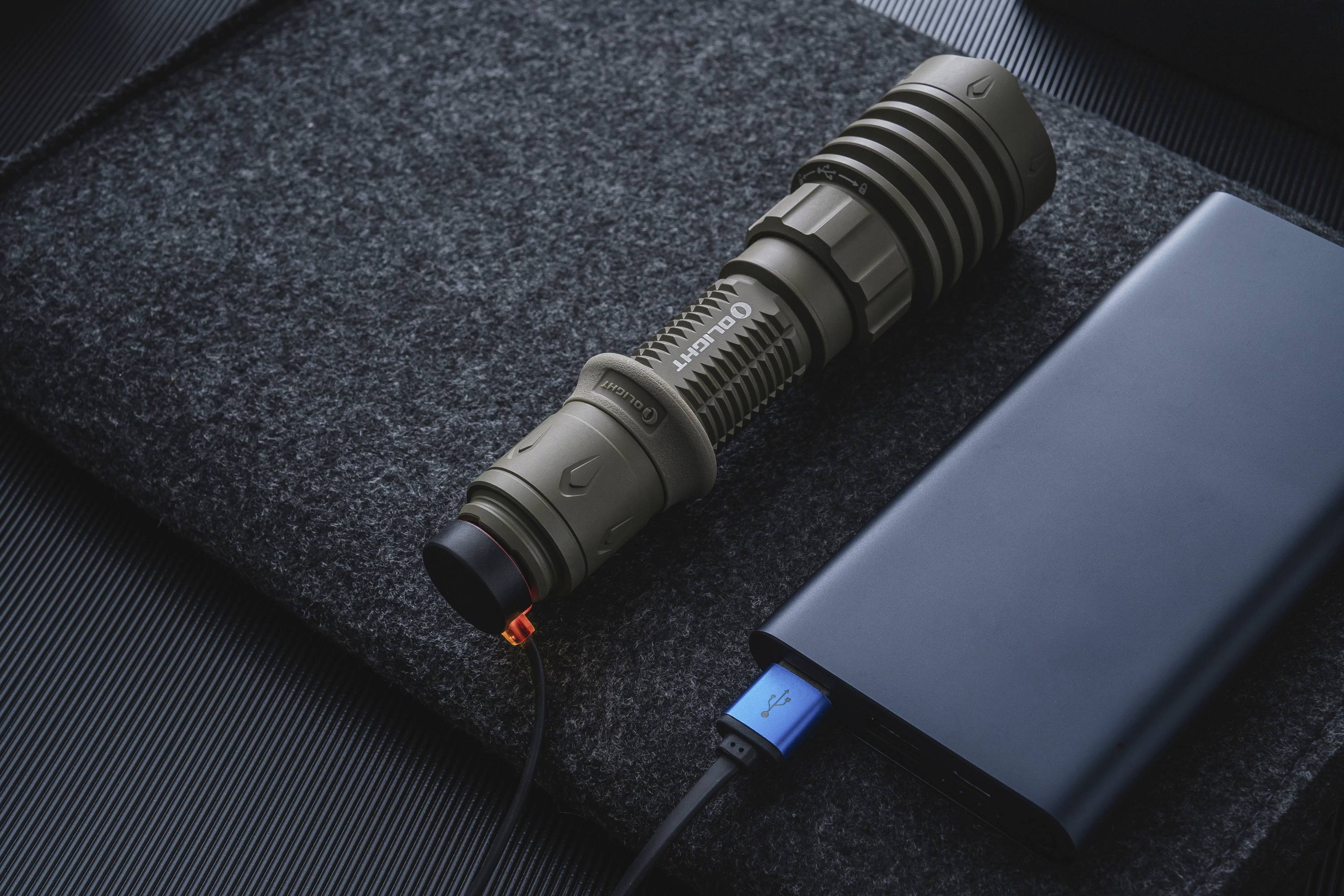 Taschenlampe wird über ein USB-Kabel mit einer Powerbank aufgeladen. Die Taschenlampe liegt auf einer dunklen Stoffoberfläche.