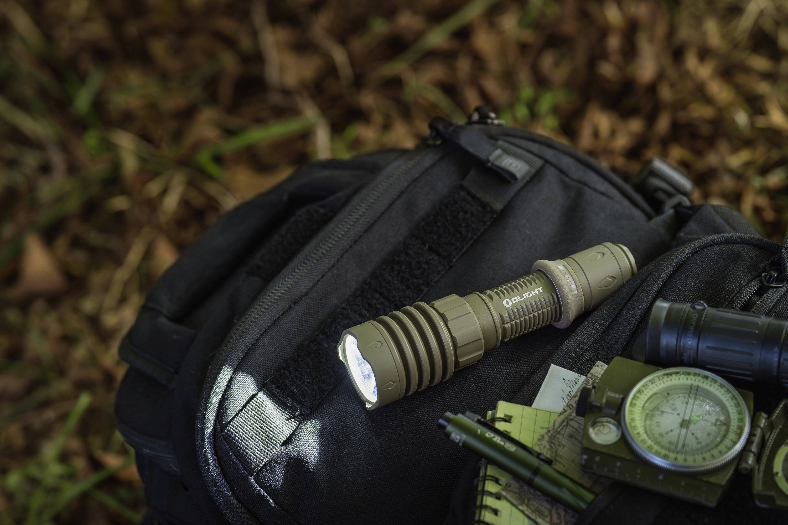 Taschenlampe auf einem schwarzen Rucksack im Wald, neben einem Kompass und Notizblock. Ideal für Outdoor-Aktivitäten.
