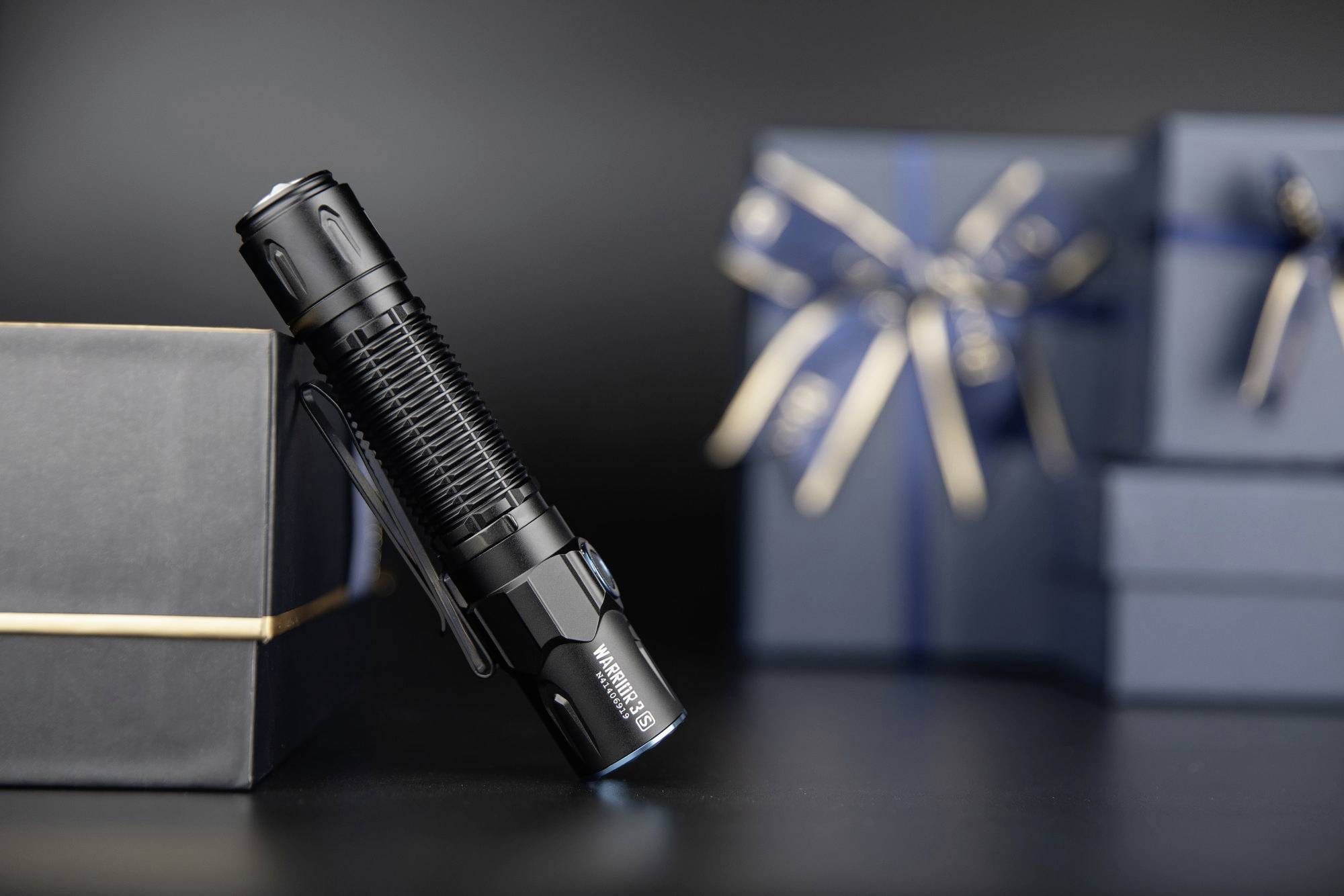 Taschenlampe lehnt an einem eleganten, dunkelblauen Geschenk mit Schleife. Im Hintergrund weitere Geschenke.