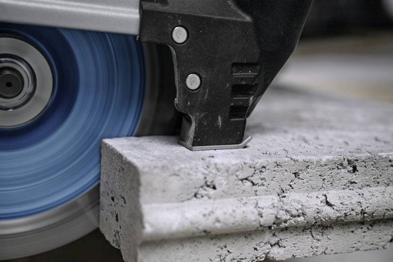 Nahaufnahme einer Kreissäge, die durch Beton schneidet. Die blaue Klinge dreht sich schnell und erzeugt Betonstaub.