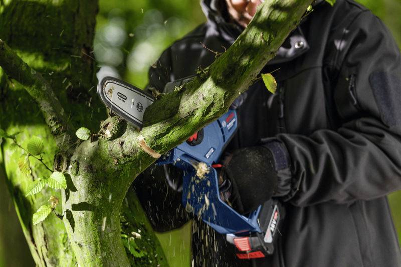 Person schneidet einen Ast mit einer handlichen Elektrosäge im Wald ab.