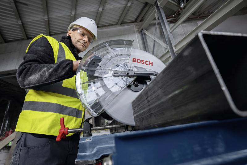Eine Person in Arbeitskleidung und Helm bedient eine Bosch-Säge in einer industriellen Umgebung.