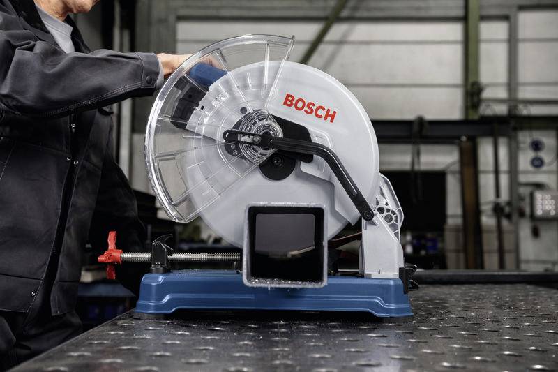 Person bedient eine Bosch-Metallsäge auf einem Tisch in einer Werkstattumgebung.